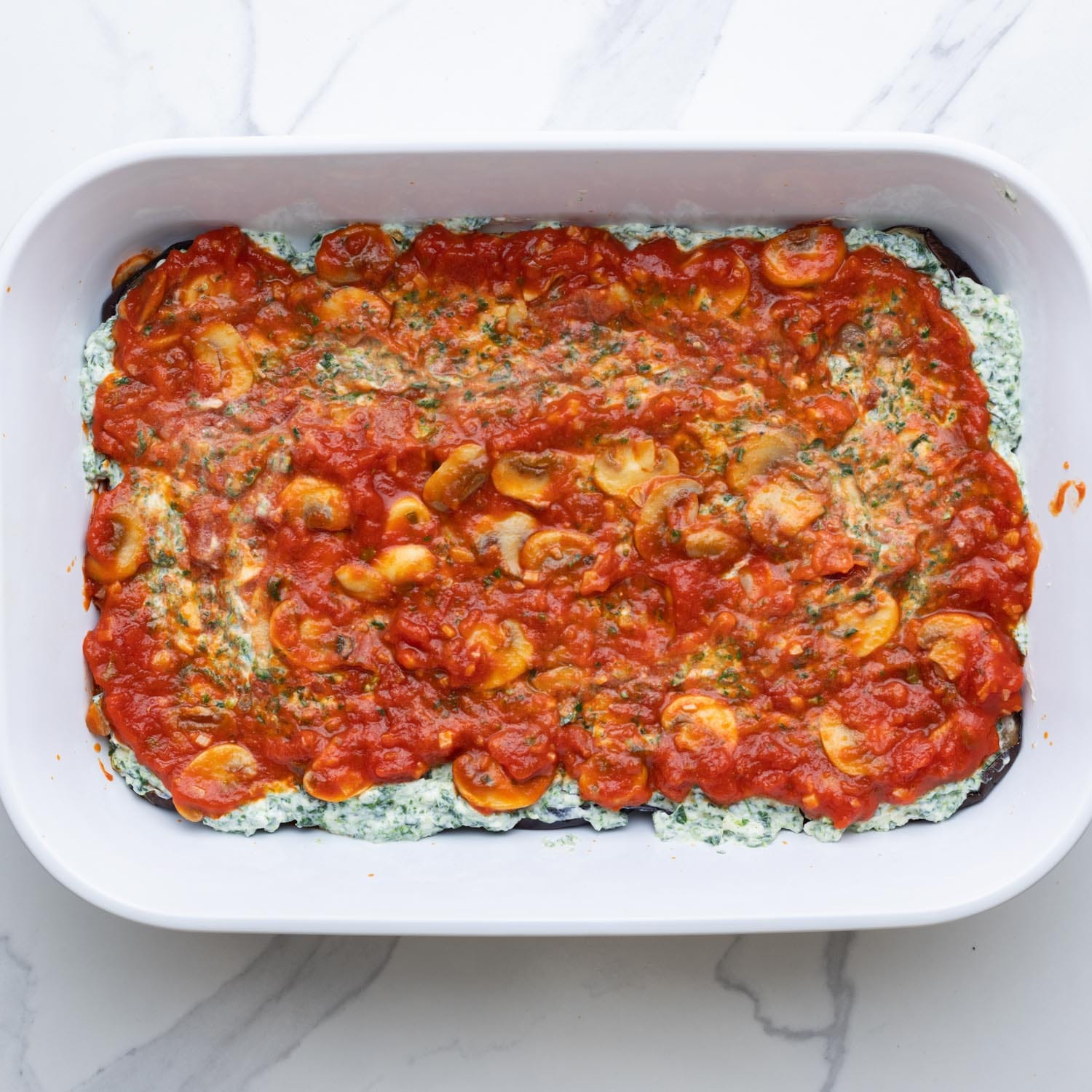 tomato sauce with mushrooms layered over ricotta cheese in a lasagna pan.