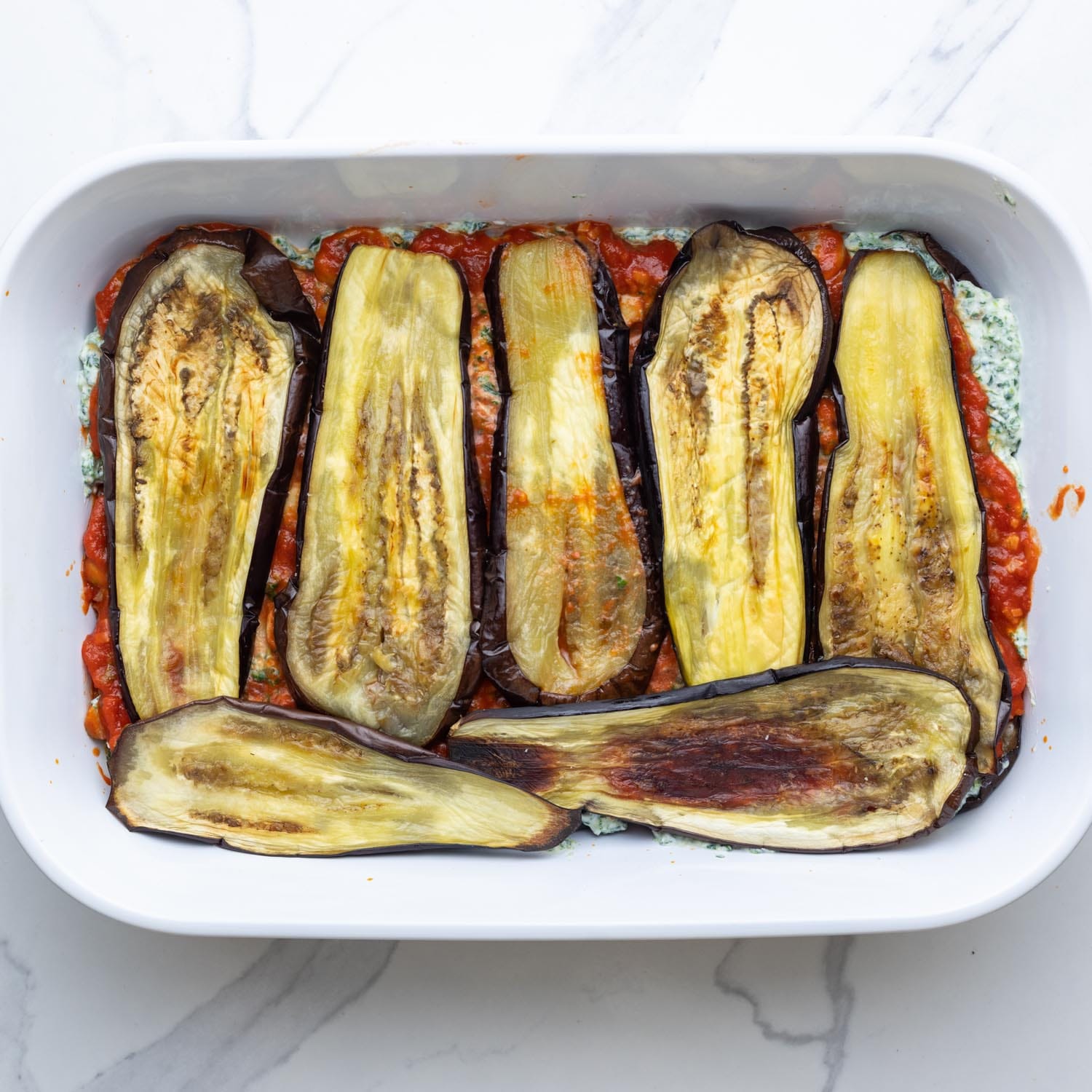 Planks of roasted eggplant layered onto sauce and cheese to make eggplant lasagna.