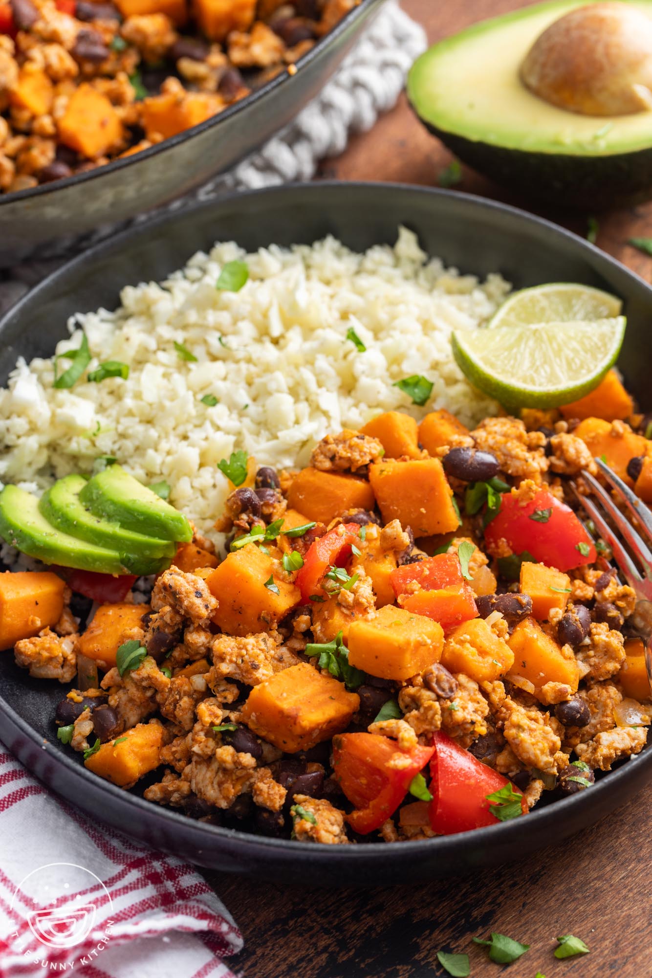 a black dinner plate. Half the plate is filled with cauliflower rice. The other half is ground turkey and sweet potato skillet with black beans and bell peppers.