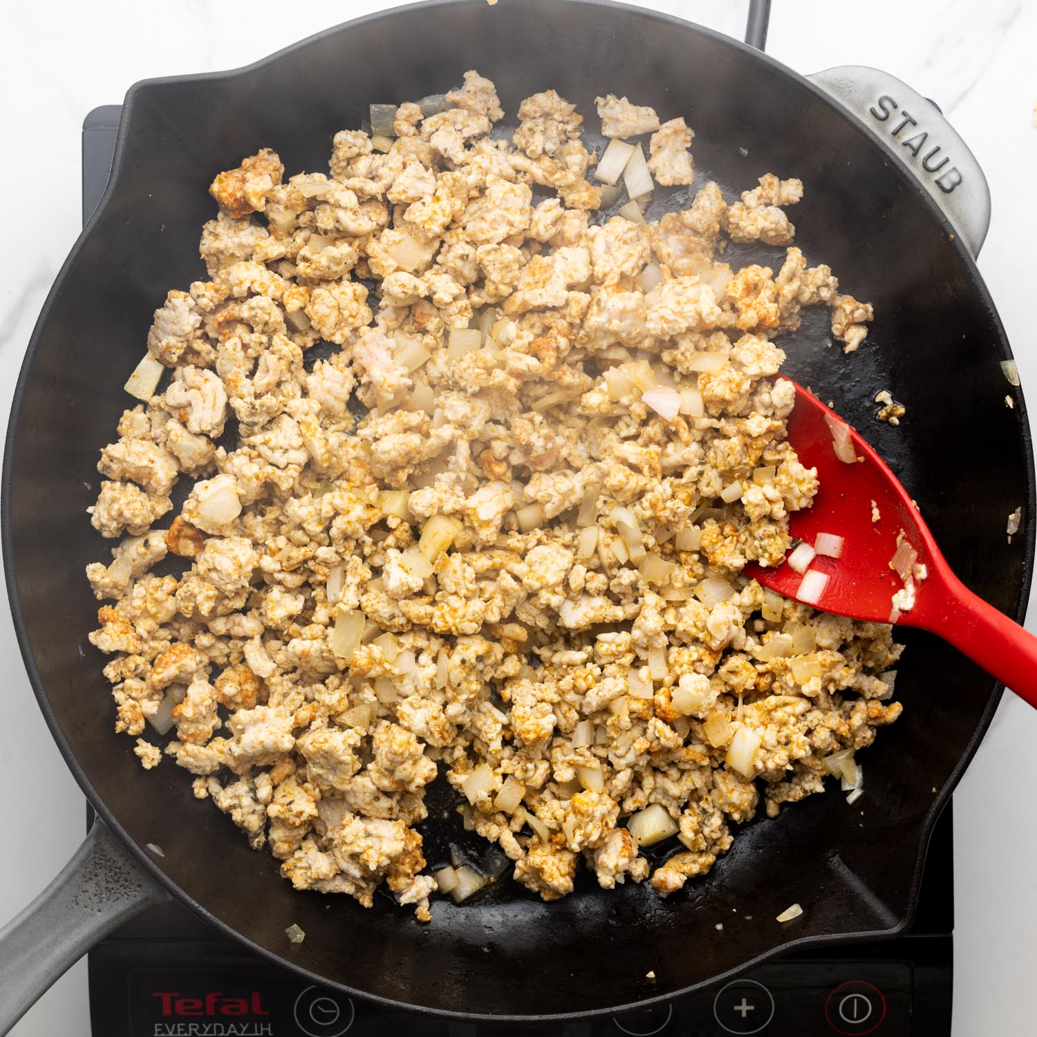 diced onion and ground turkey cooking in a skillet, with a red spatula.