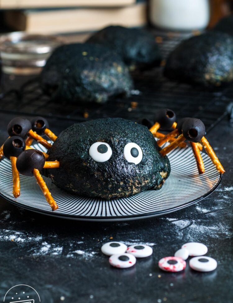 a buffalo chicken bomb which is buffalo chicken and cheese inside a pizza dough ball, decorated black and with pretzel and olive leggs to look like a large spider. The bomb is sitting on a black and white striped plate.