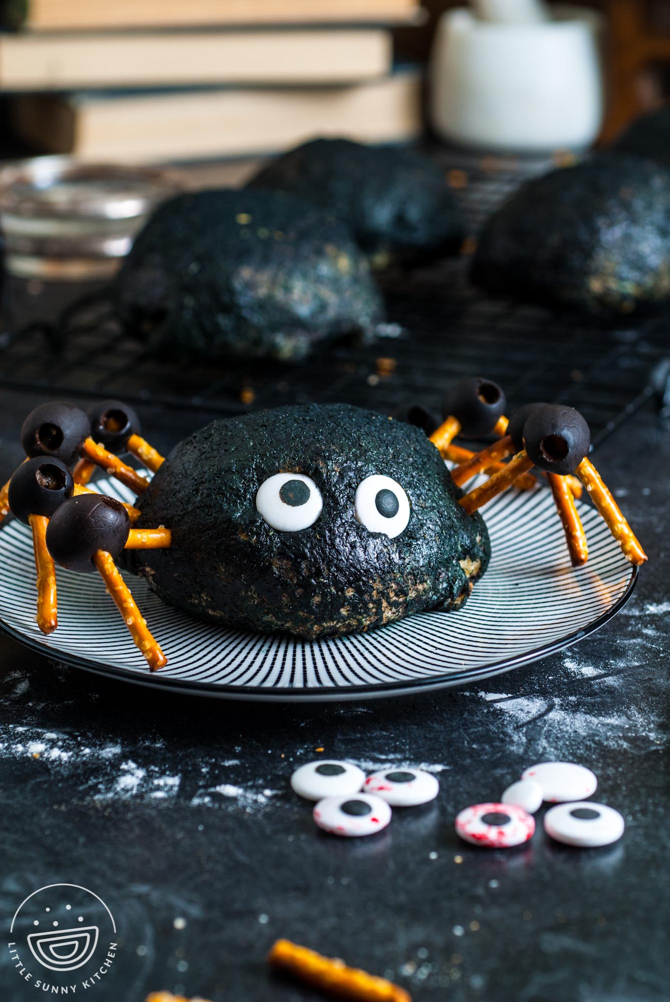 a buffalo chicken bomb which is buffalo chicken and cheese inside a pizza dough ball, decorated black and with pretzel and olive leggs to look like a large spider. The bomb is sitting on a black and white striped plate.