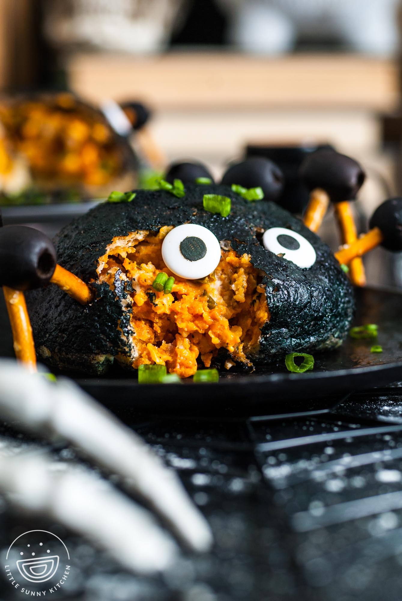 a black buffalo chicken stuffed pizza bomb with pretzel legs and eyes to look like a spider. A bite is taken from the front of the face.