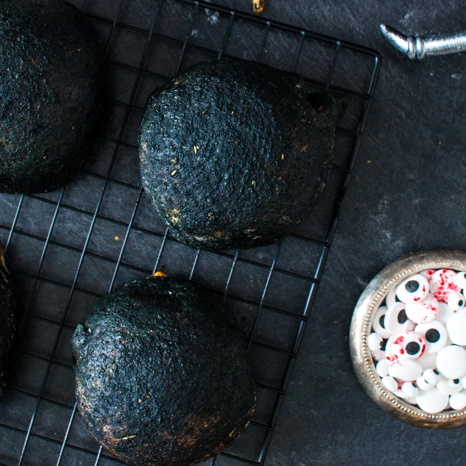 baked buffalo chicken bombs that are dyed black for halloween, next to a boil of halloween candy eyes.