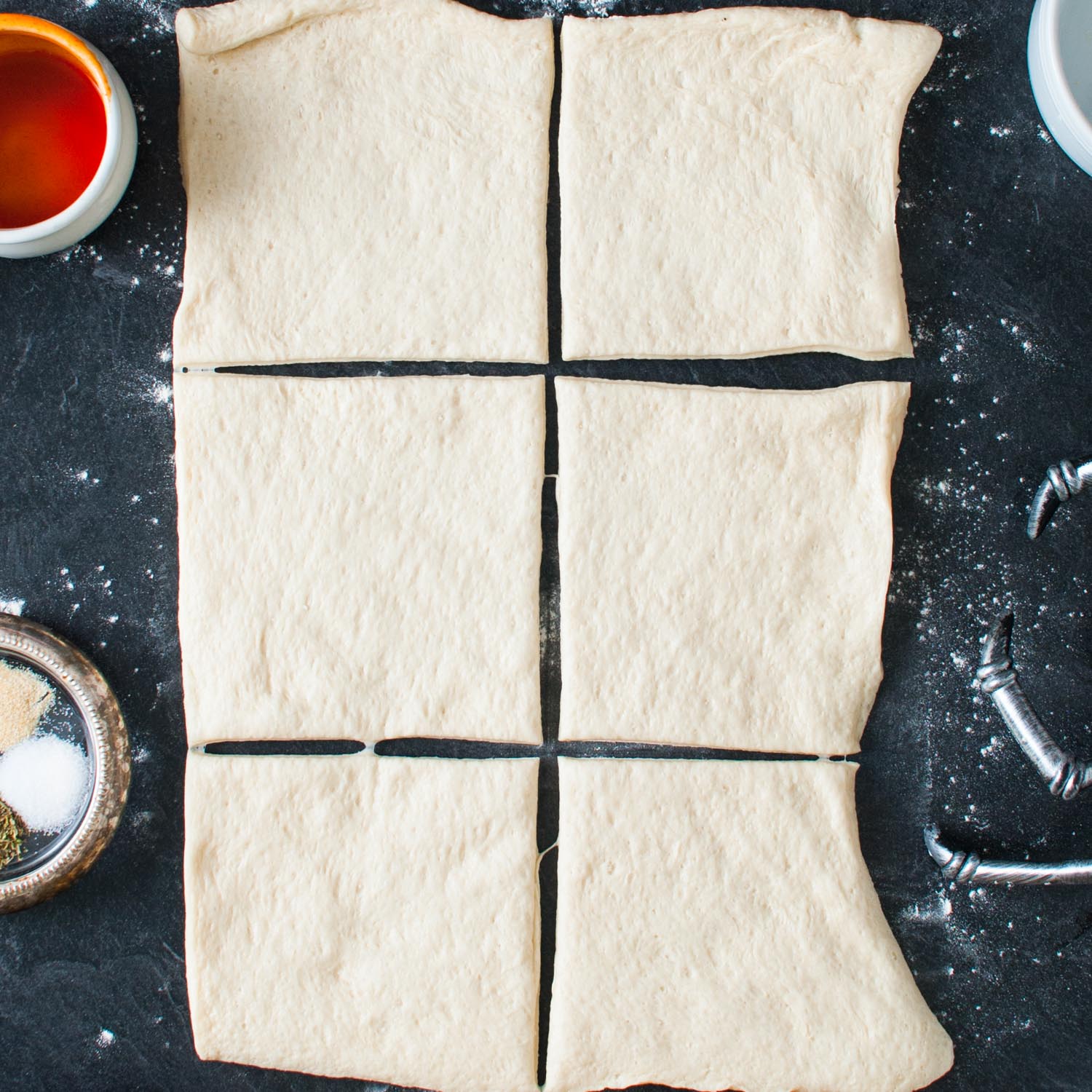 pizza dough rolled out on a black surface into a rectangle that has been cut into 6 squares.