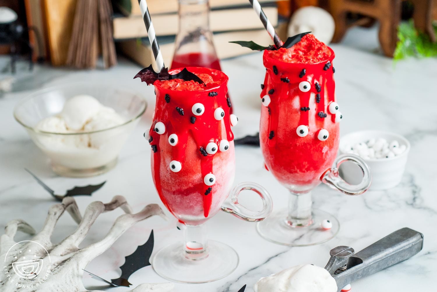 Two bloody red vampire floats on a table. Around the drinks are halloween decorations.