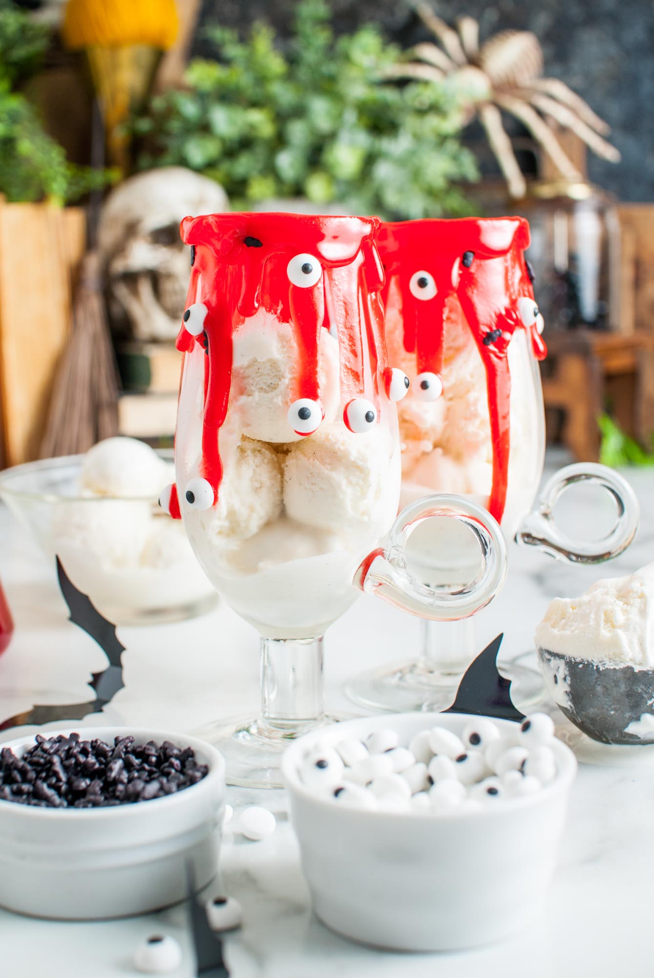 Vanilla ice cream added to two milkshake glasses that have been decorated to look spooky with red icing and candy eyes.