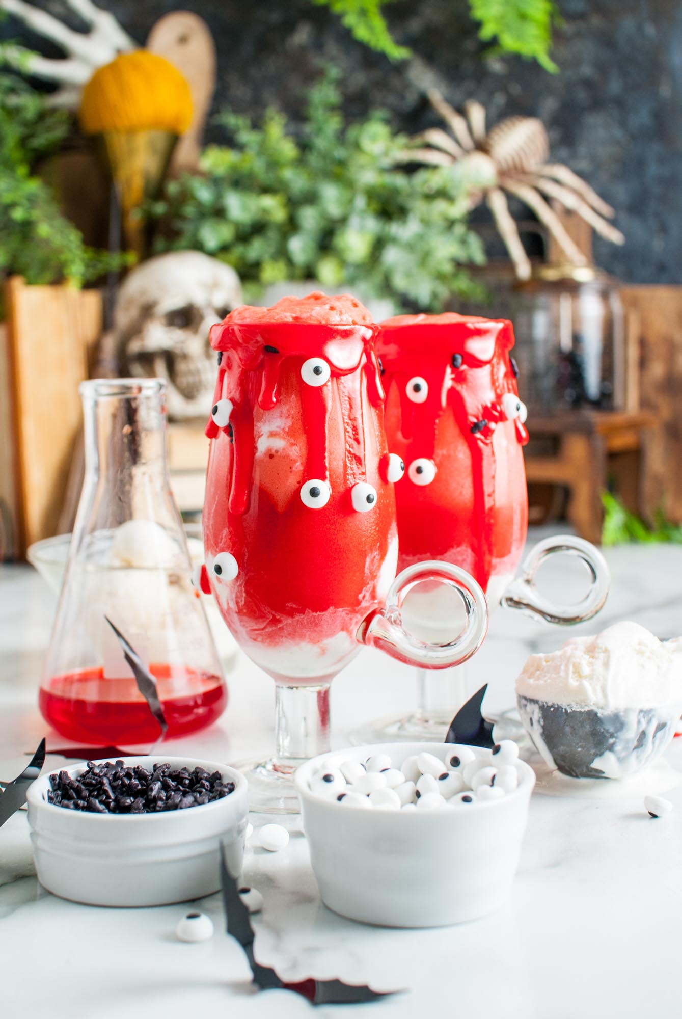 two halloween vampire floats made in footed glass mugs. The glasses are rimmed with red icing and spooky sprinkles.