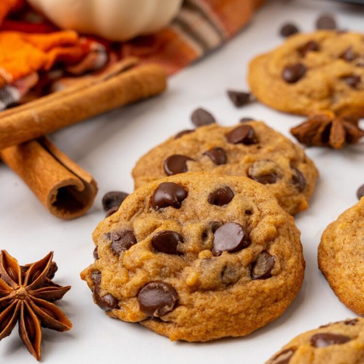 chocolate chip cookies made with pumpkin on a counter. In the background are small pumpkins and an orange towel.