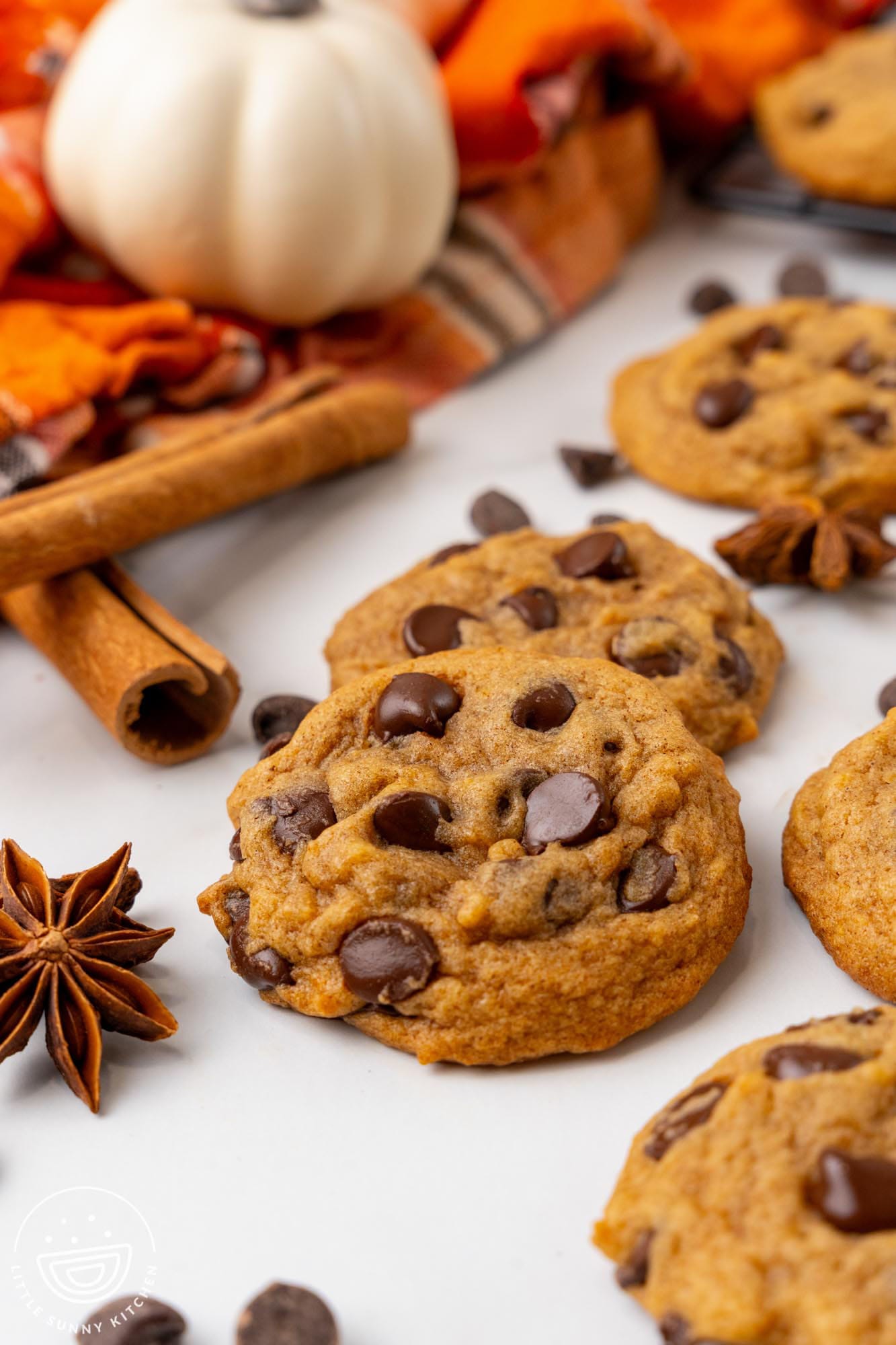 chocolate chip cookies made with pumpkin on a counter. In the background are small pumpkins and an orange towel.