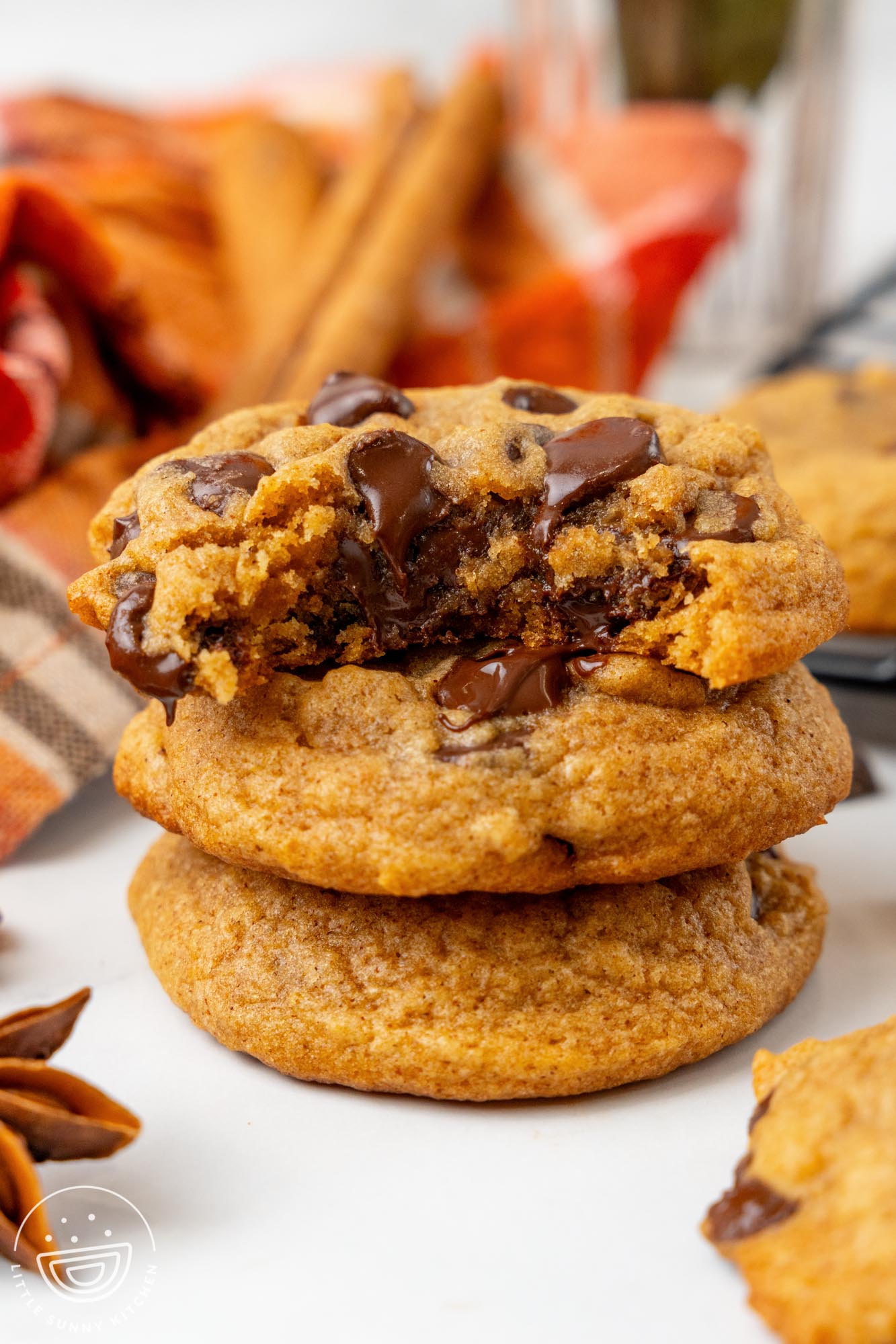 a stack of three pumpkin chocolate chip cookies. The top cookie has a bite removed, showing the melty chocolate inside.