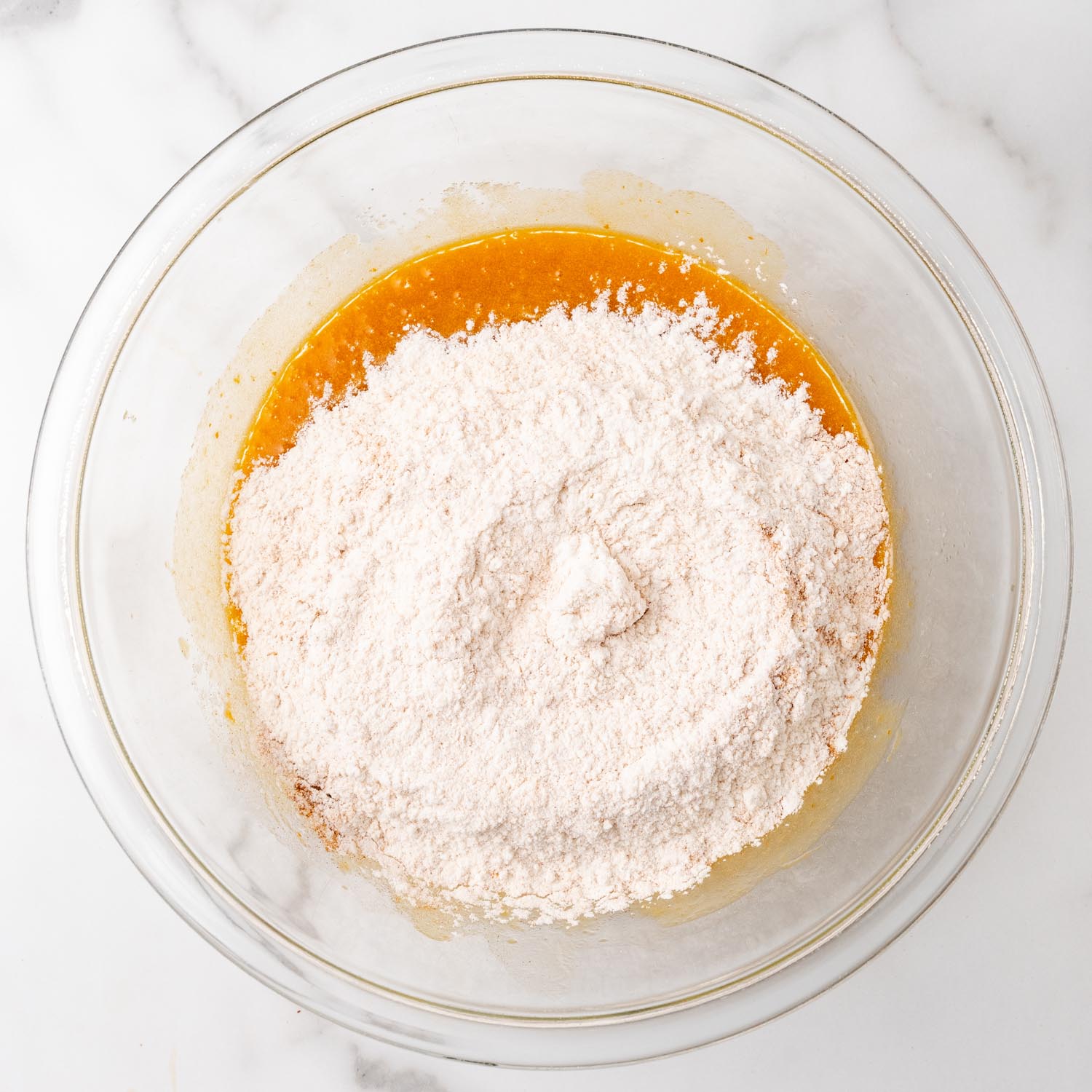 flour added to pumpkin puree mixture in a glass mixing bowl.