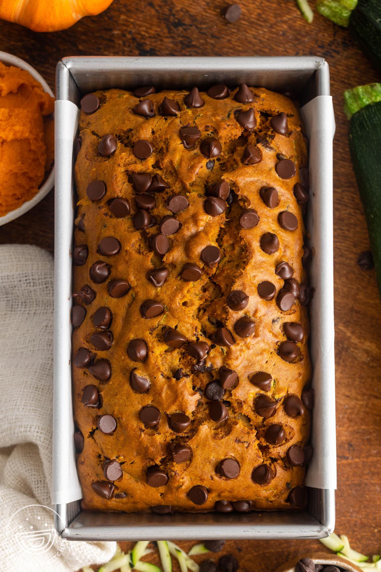 a baked loaf of pumpkin zucchini bread with chocolate chips in a metal loaf pan.