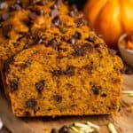 sliced loaf of pumpkin zucchini bread with chocolate chips on a wooden board.