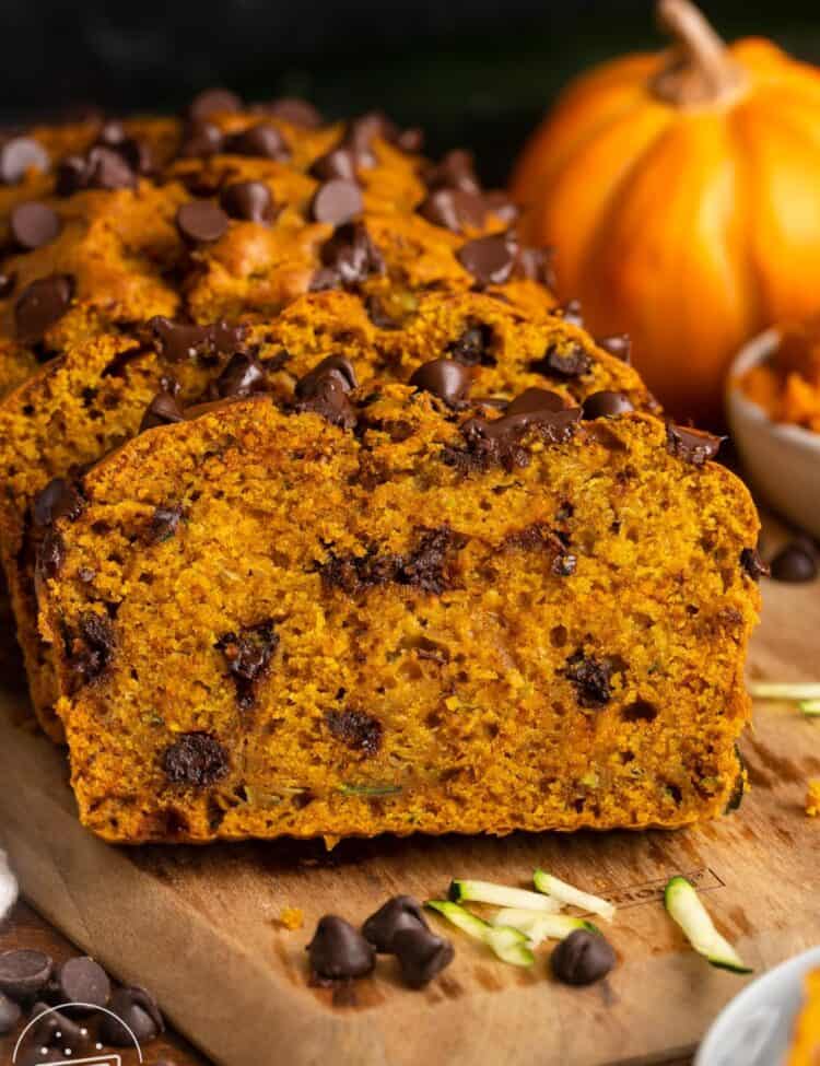 sliced loaf of pumpkin zucchini bread with chocolate chips on a wooden board.