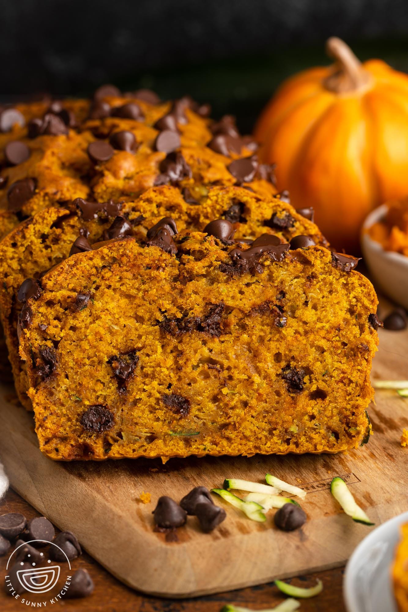 sliced loaf of pumpkin zucchini bread with chocolate chips on a wooden board.