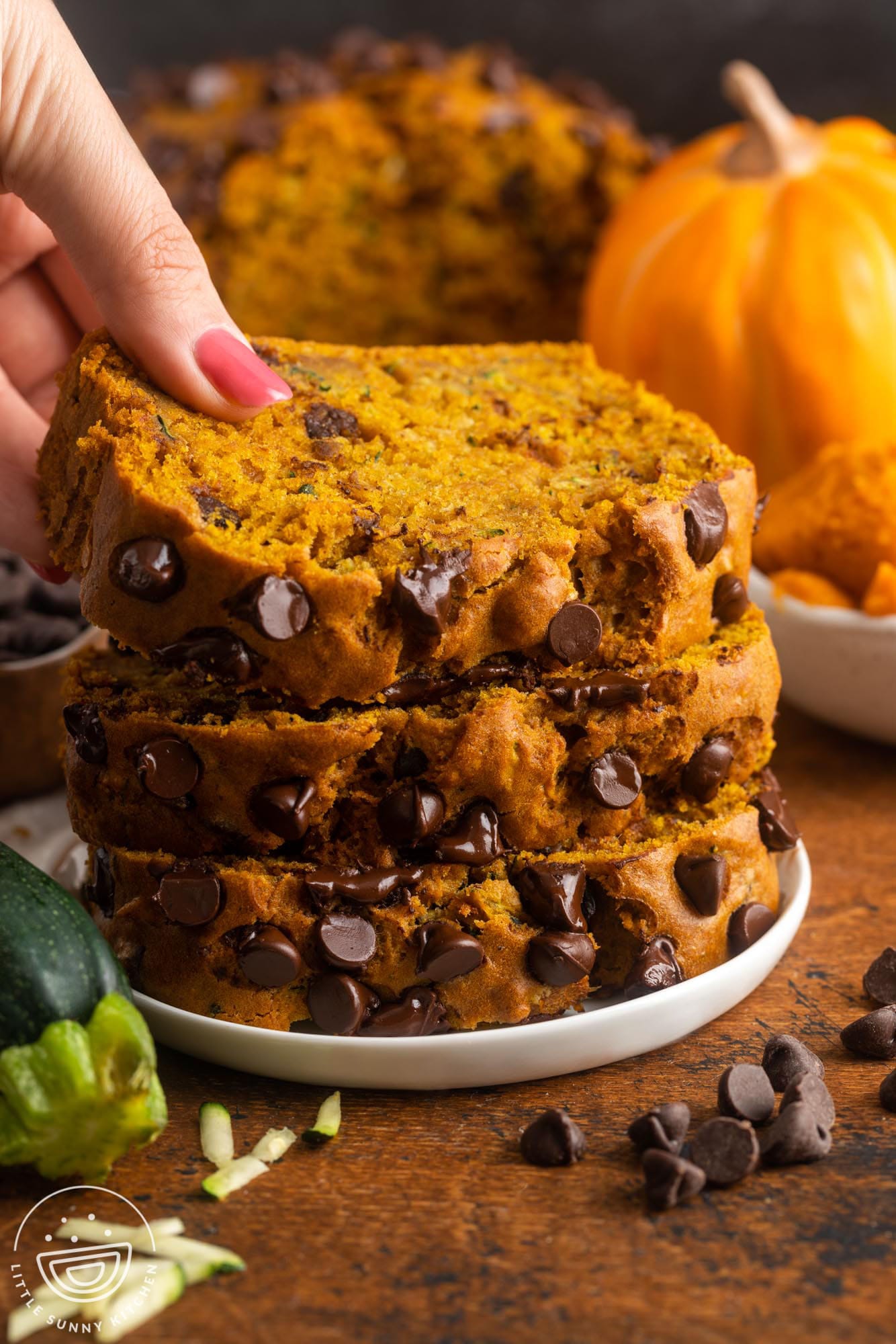 three thick slices of pumpkin zucchini bread with extra chocolate chips. A hand is picking up the slice on top.