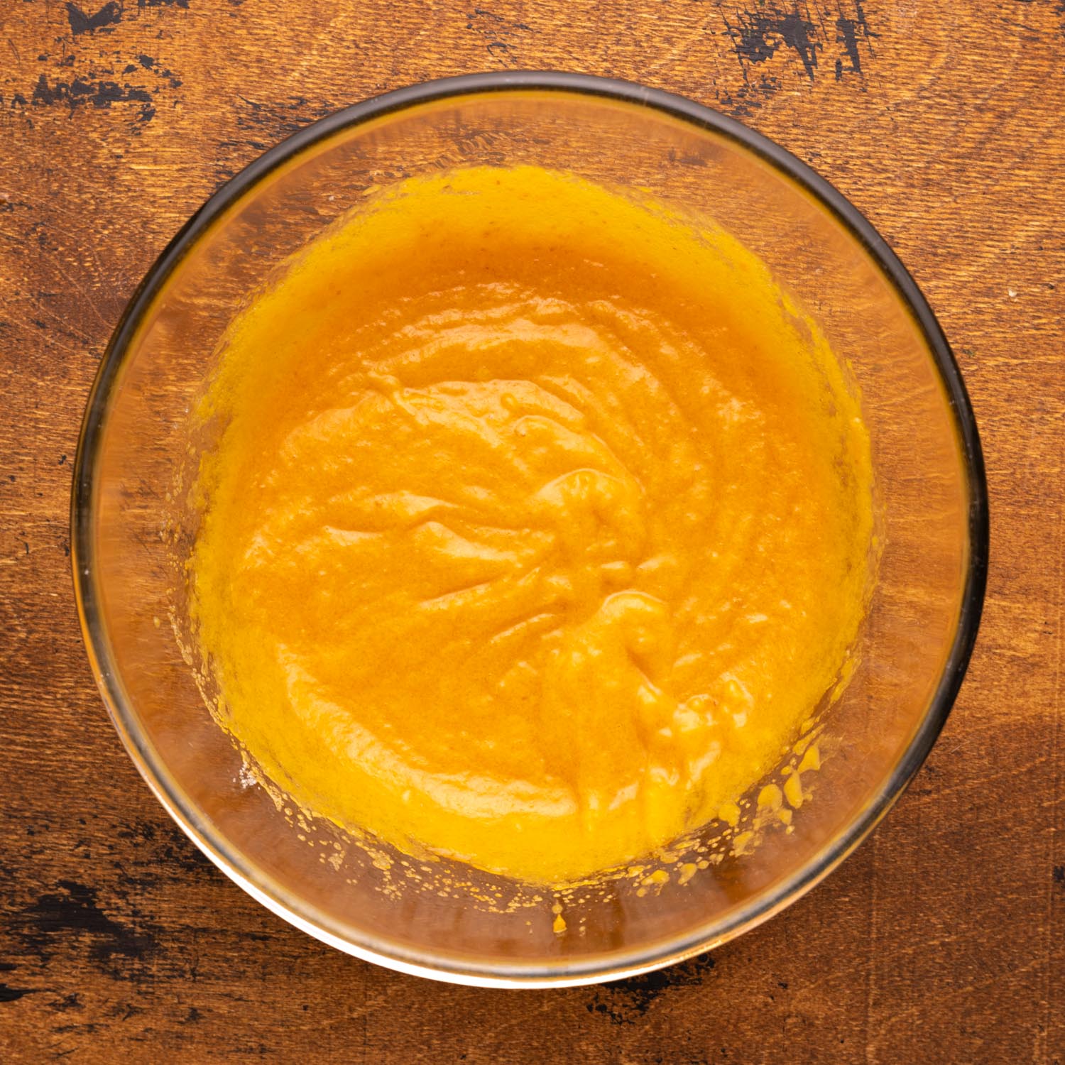 pumpkin puree mixed with sugar, oil, and eggs in a metal mixing bowl on a wooden surface.