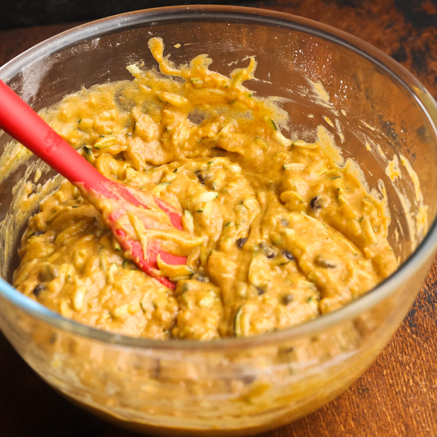 pumpkin zucchini bread batter stirred in a glass bowl with a red spatula.