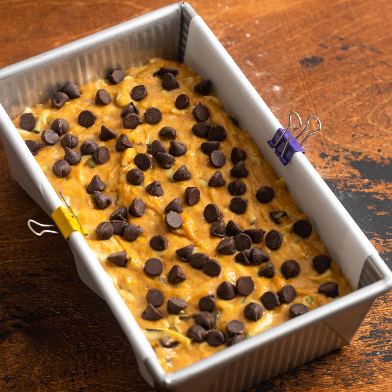 pumpkin zucchini bread batter in a rectangular bread pan that is lined with parchment paper. Chocolate chips are added to the top.