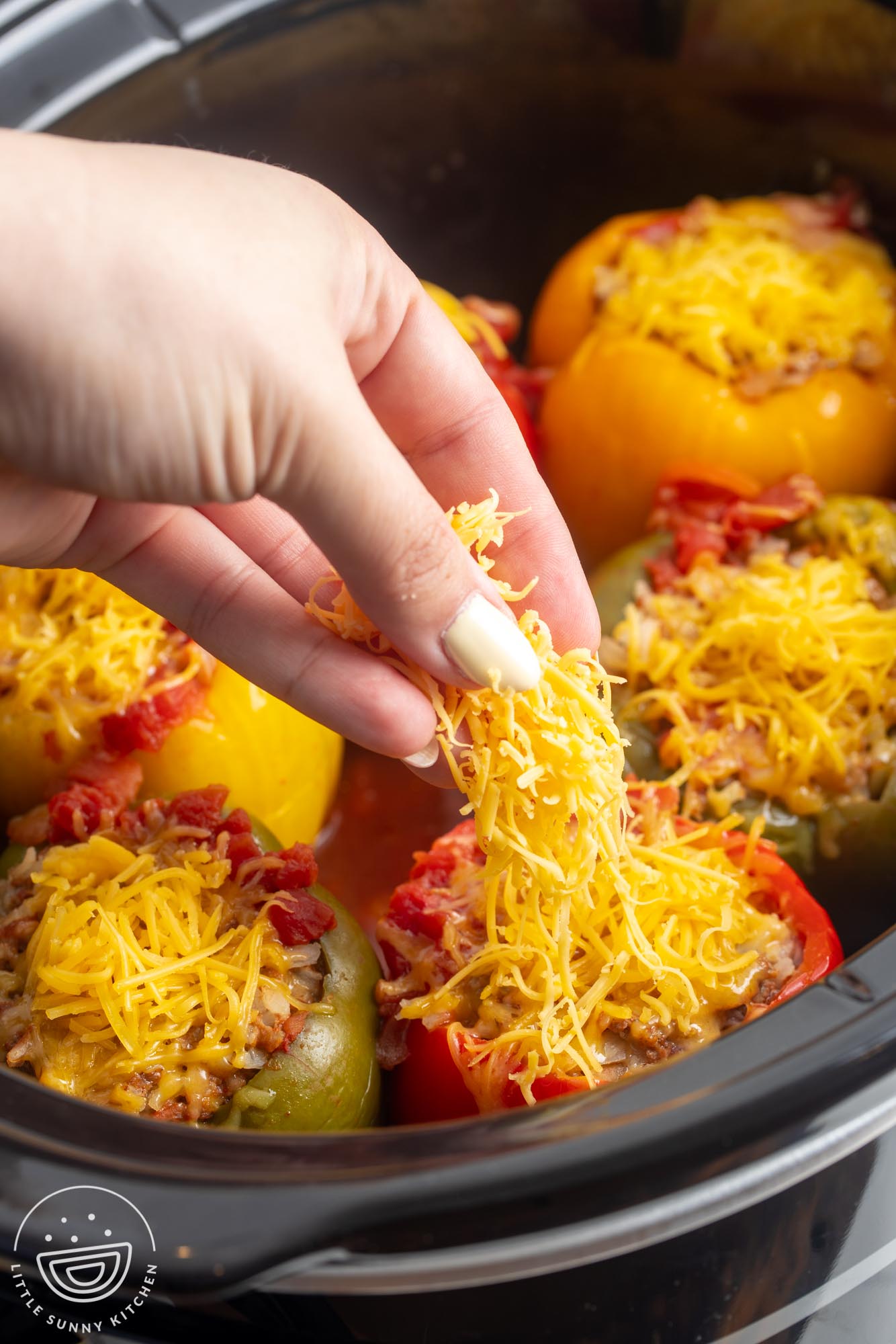 a hand adding shredded cheese to stuffed peppers in a crock pot.