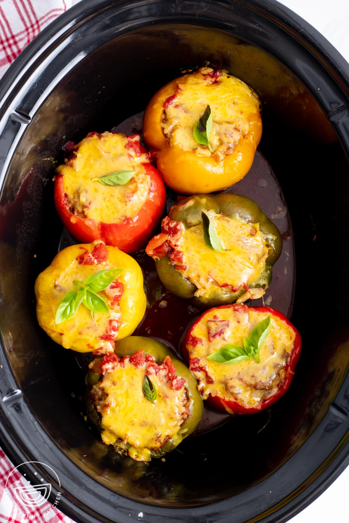 cheesy stuffed peppers in a slow cooker, garnished with basil for serving.