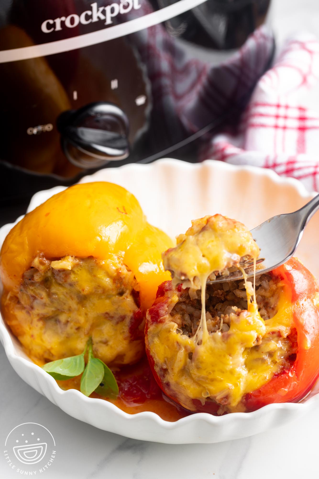 one yellow and one red stuffed pepper in a white bowl. A fork is eating the filling from the red one.