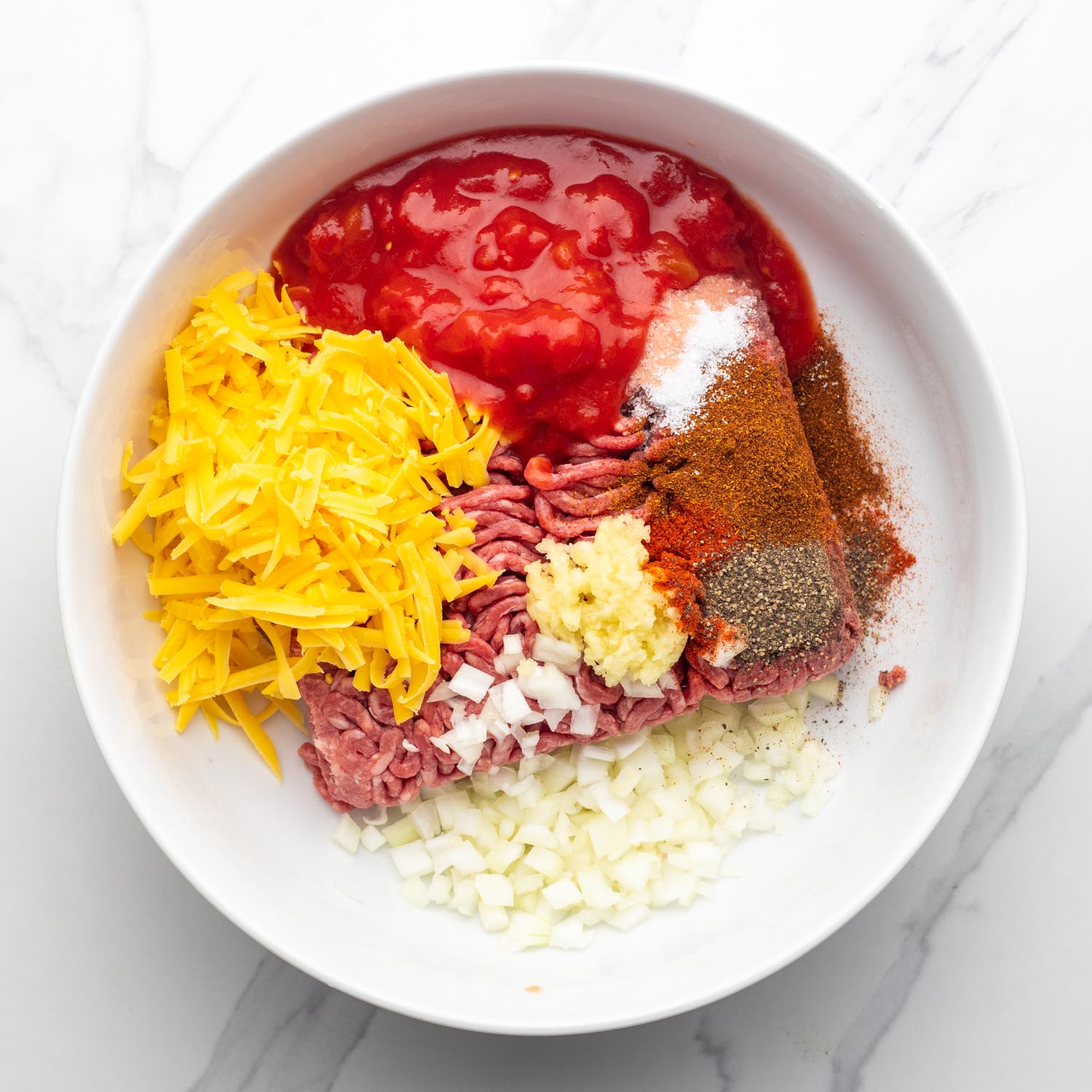 stuffed pepper ingredients, meat, seasonings, onions, cheese, tomato sauce, in a white bowl.