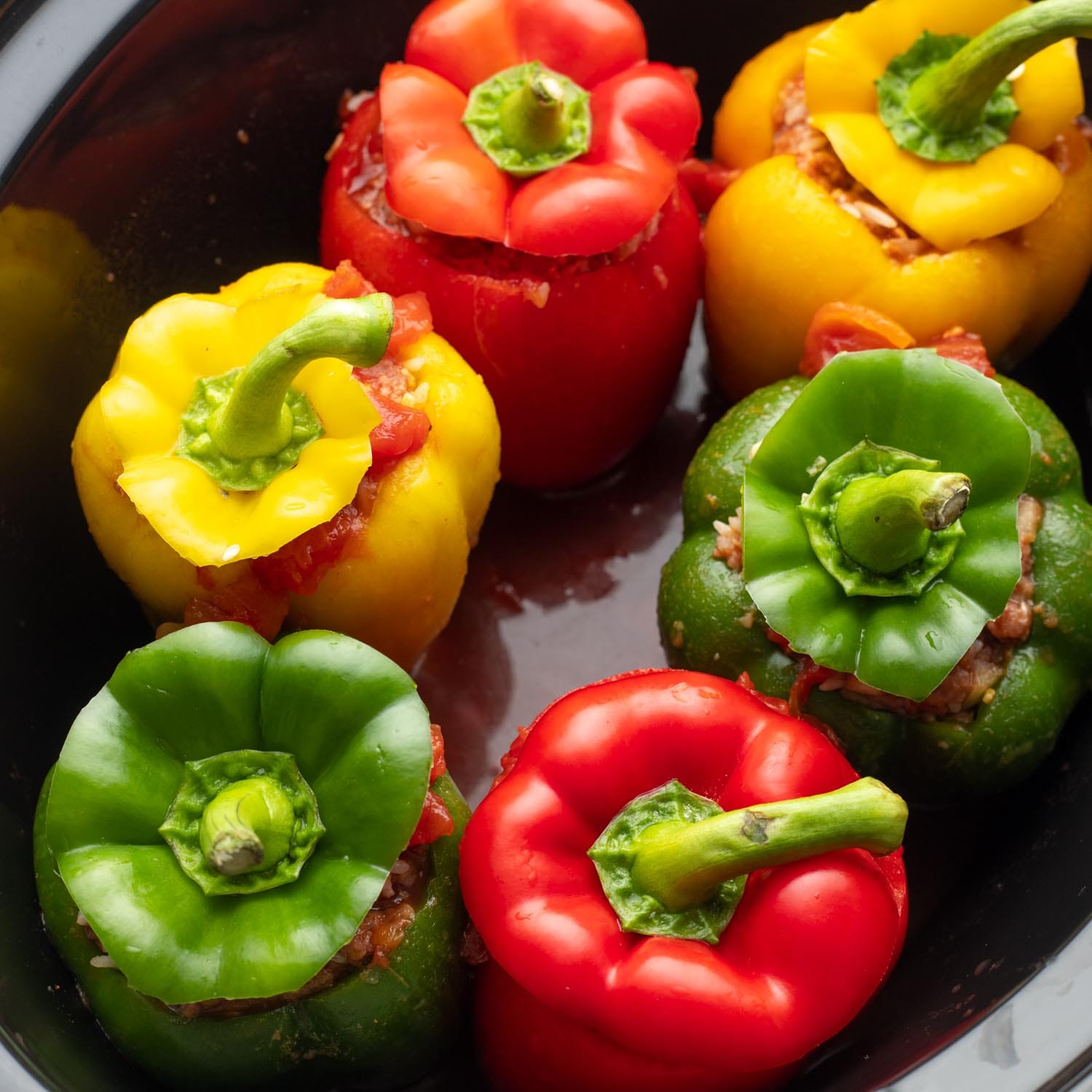 Stuffed peppers in a slow cooker. The tops have been placed back on the peppers.