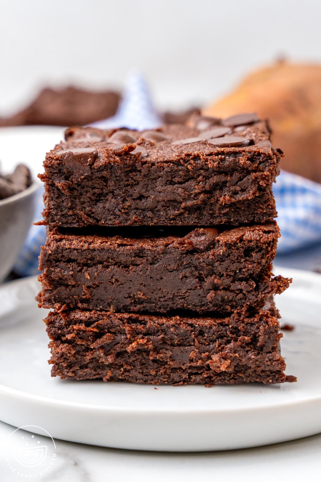 three stacked dense chocolate sweet potato brownies on a white plate.