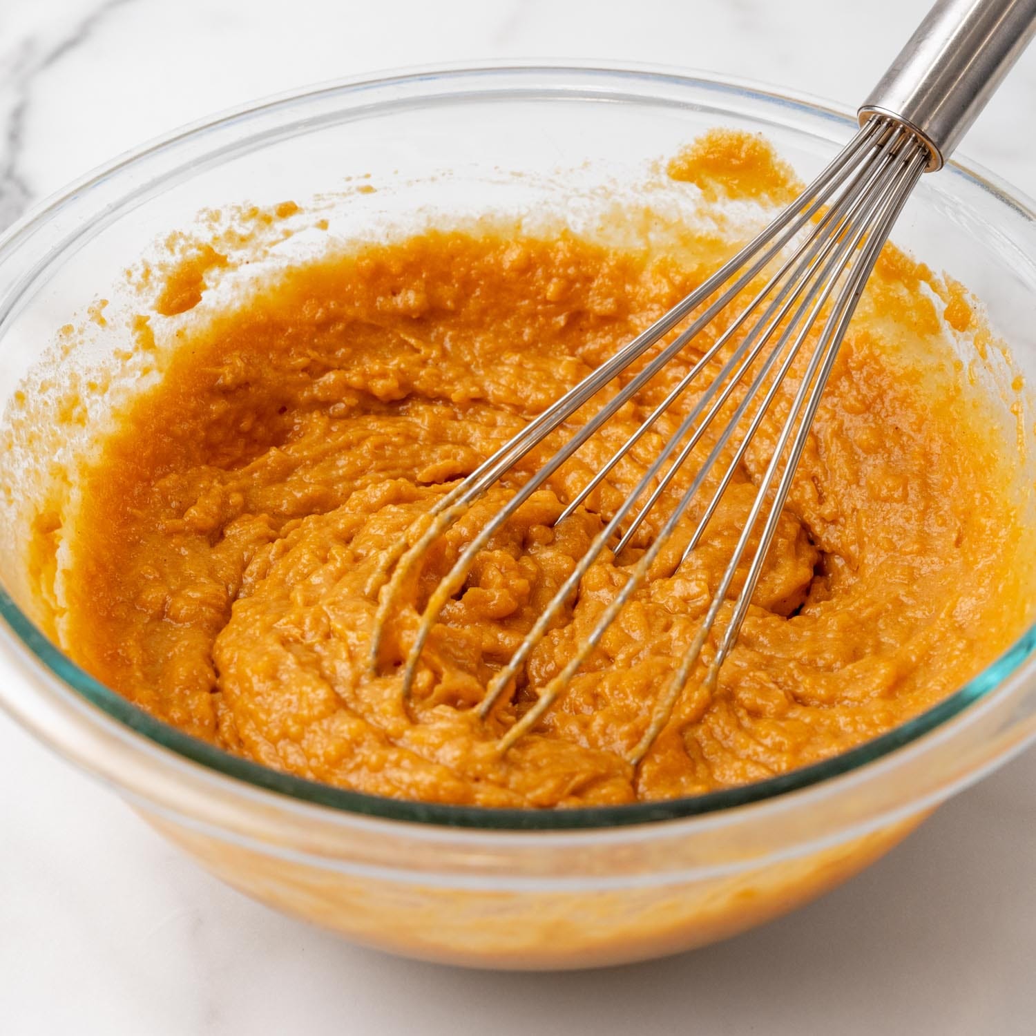 pureed sweet potato in a bowl with a metal whisk.