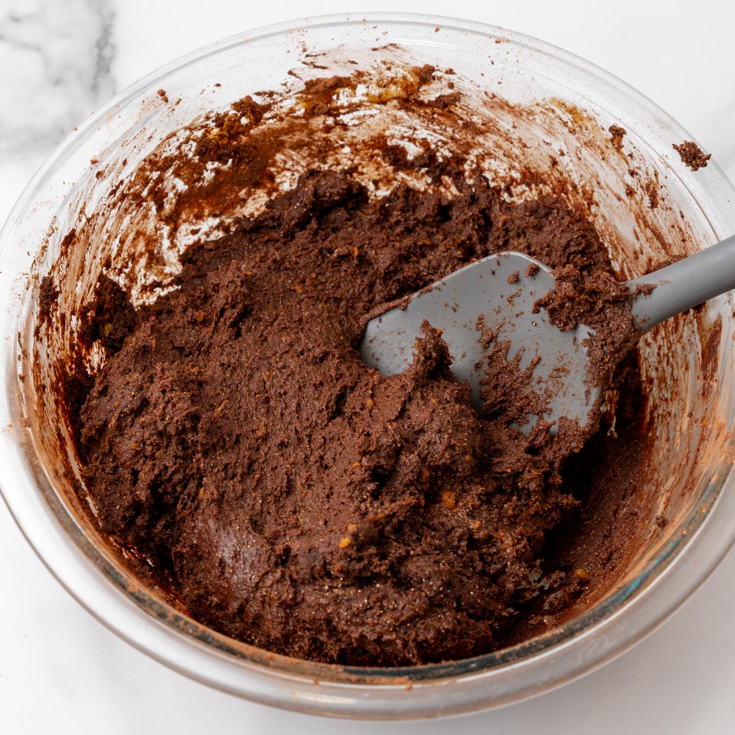 thick sweet potato brownie batter in a glass bowl stirred with a gray plastic spatula.