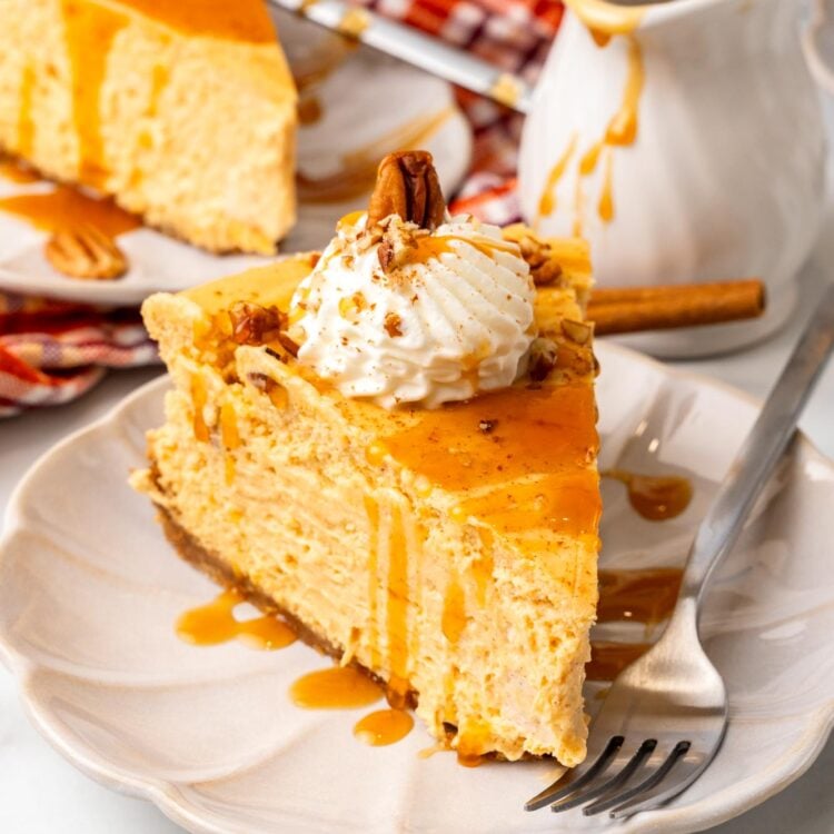 a dessert plate holding a metal fork and a slice of sweet potato cheesecake with whipped cream. in the background is a small pitcher of caramel sauce and another slice of cheesecake.