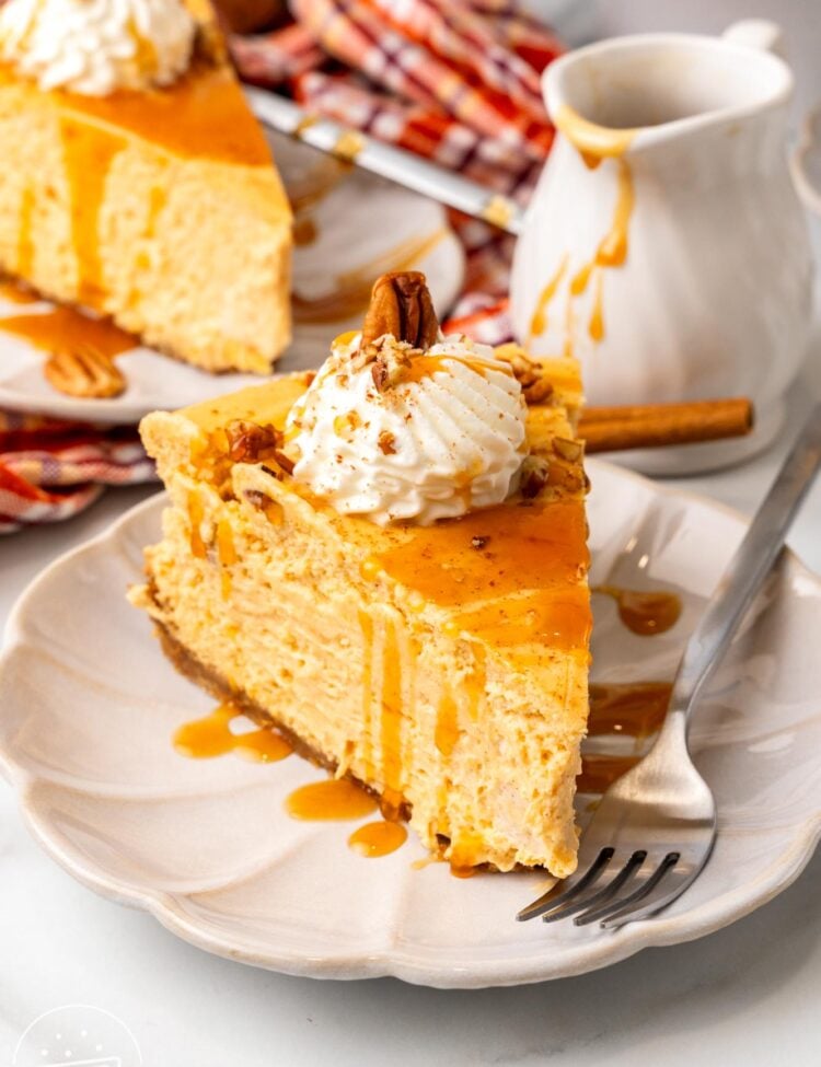 a dessert plate holding a metal fork and a slice of sweet potato cheesecake with whipped cream. in the background is a small pitcher of caramel sauce and another slice of cheesecake.