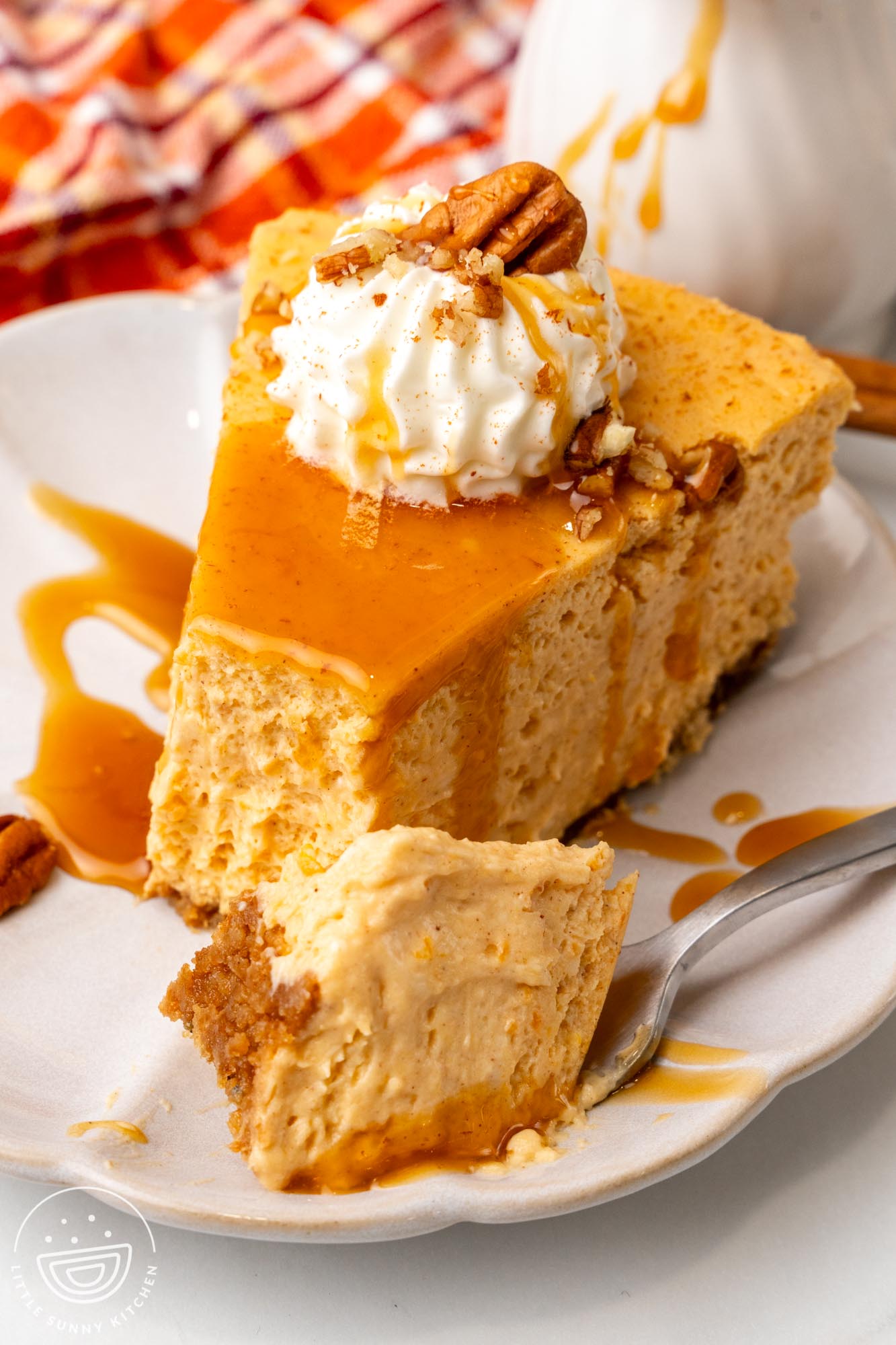 a slice of fluffy sweet potato cheesecake topped with whipped cream and pecans on a plate. One bite has been removed from the front with a fork to show the texture.