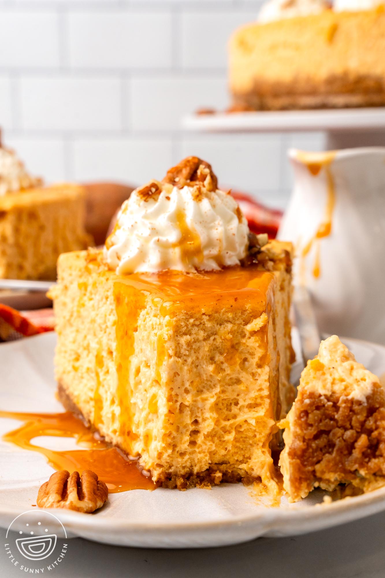 a slice of fluffy sweet potato cheesecake topped with whipped cream and pecans on a plate. One bite has been removed from the front to show the texture.