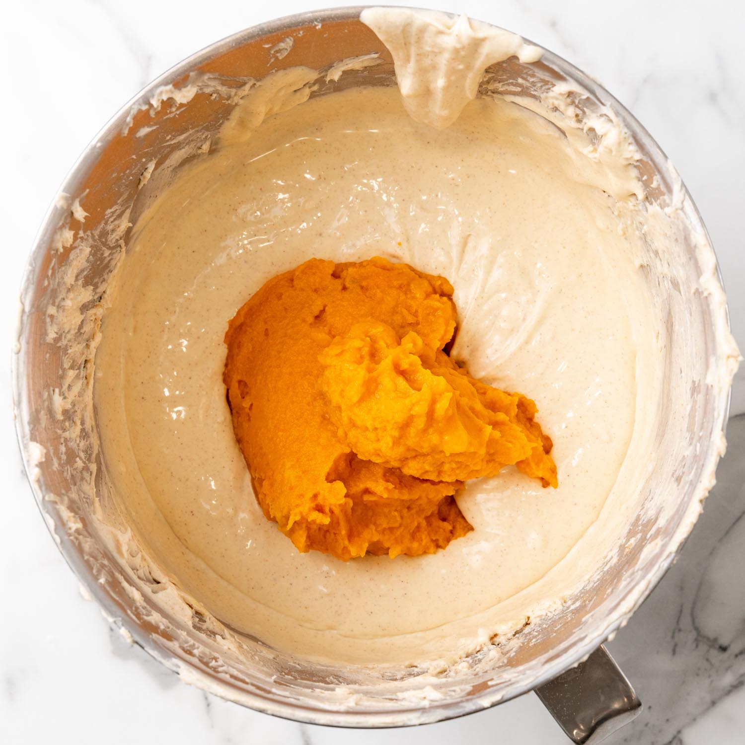 mashed sweet potato added to cheesecake batter in a metal mixing bowl.