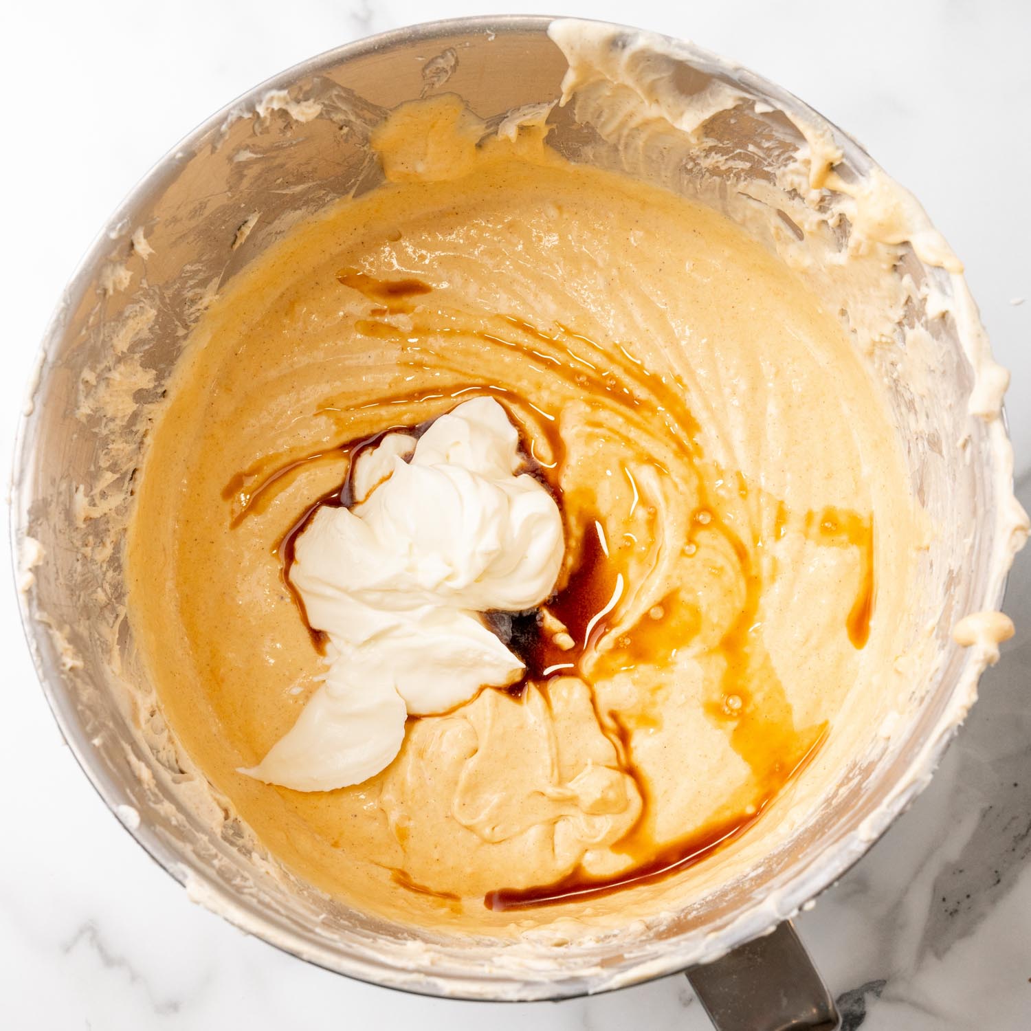 Sour cream and vanilla added to sweet potato cheesecake batter in a mixing bowl.