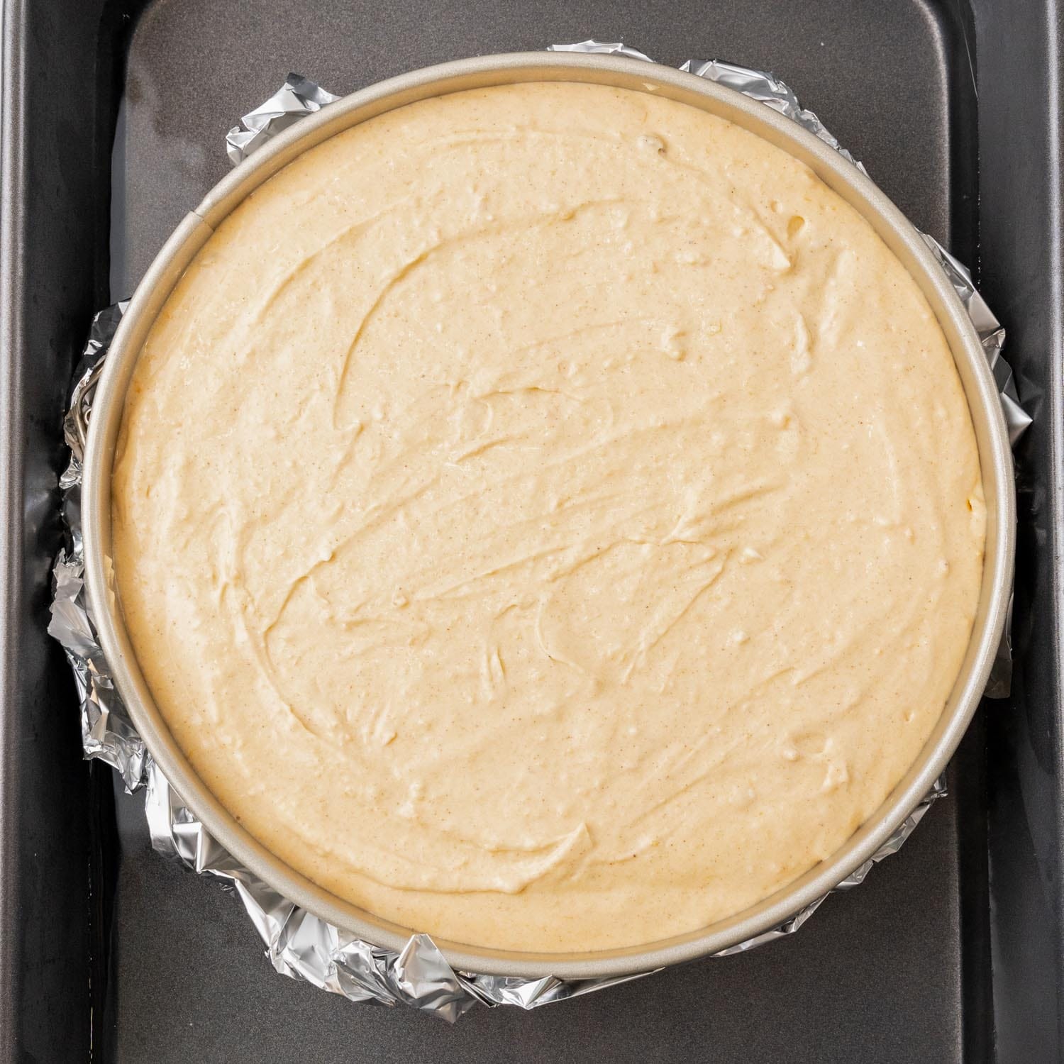 unbaked sweet potato cheesecake in a springform pan, wrapped with foil, placed in a roasting pan of water to create a waterbath.