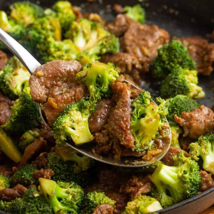 sliced beef and broccoli stir fry in a cast iron skillet, served with a large spoon.