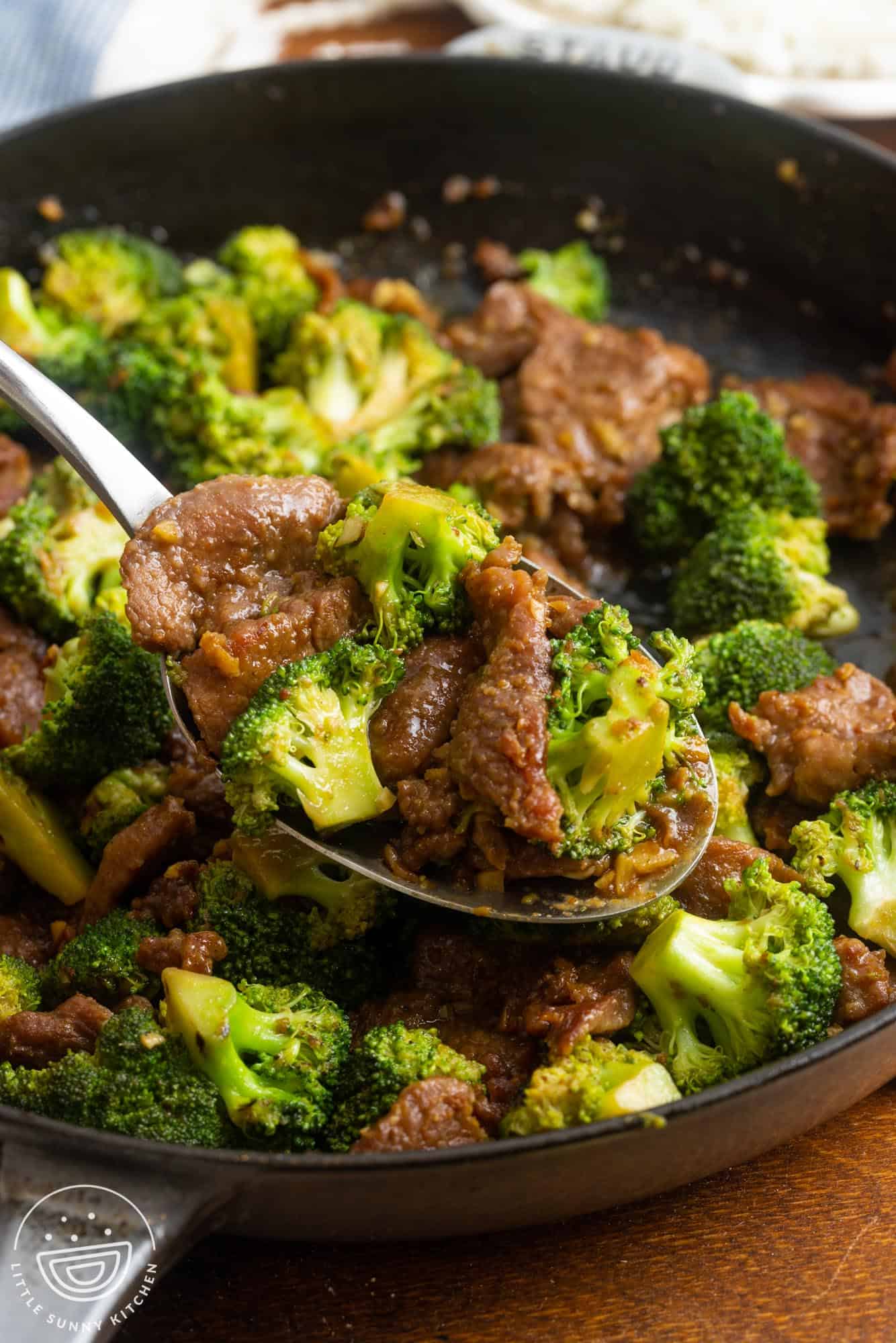 sliced beef and broccoli stir fry in a cast iron skillet, served with a large spoon.