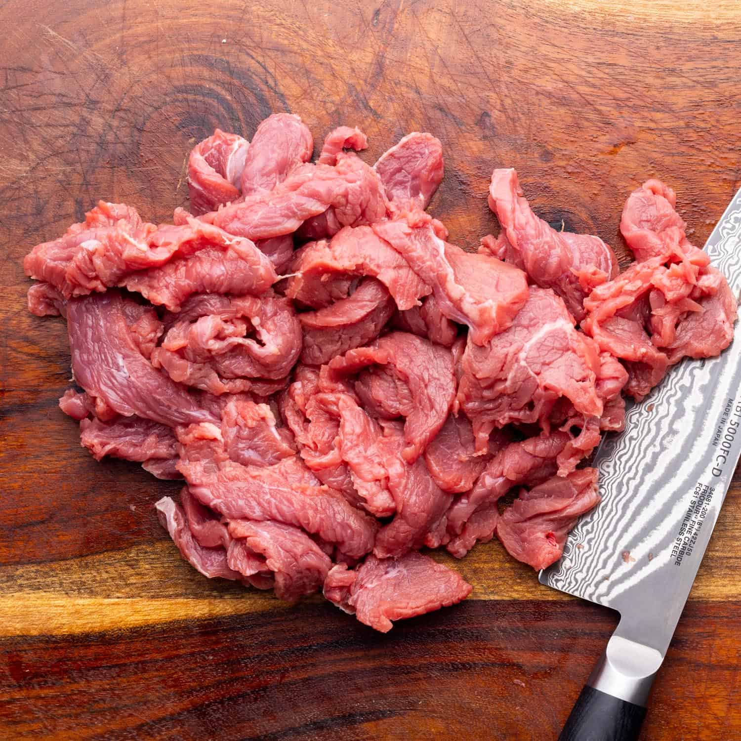 very thinly sliced beef on a cutting board with a chefs knife