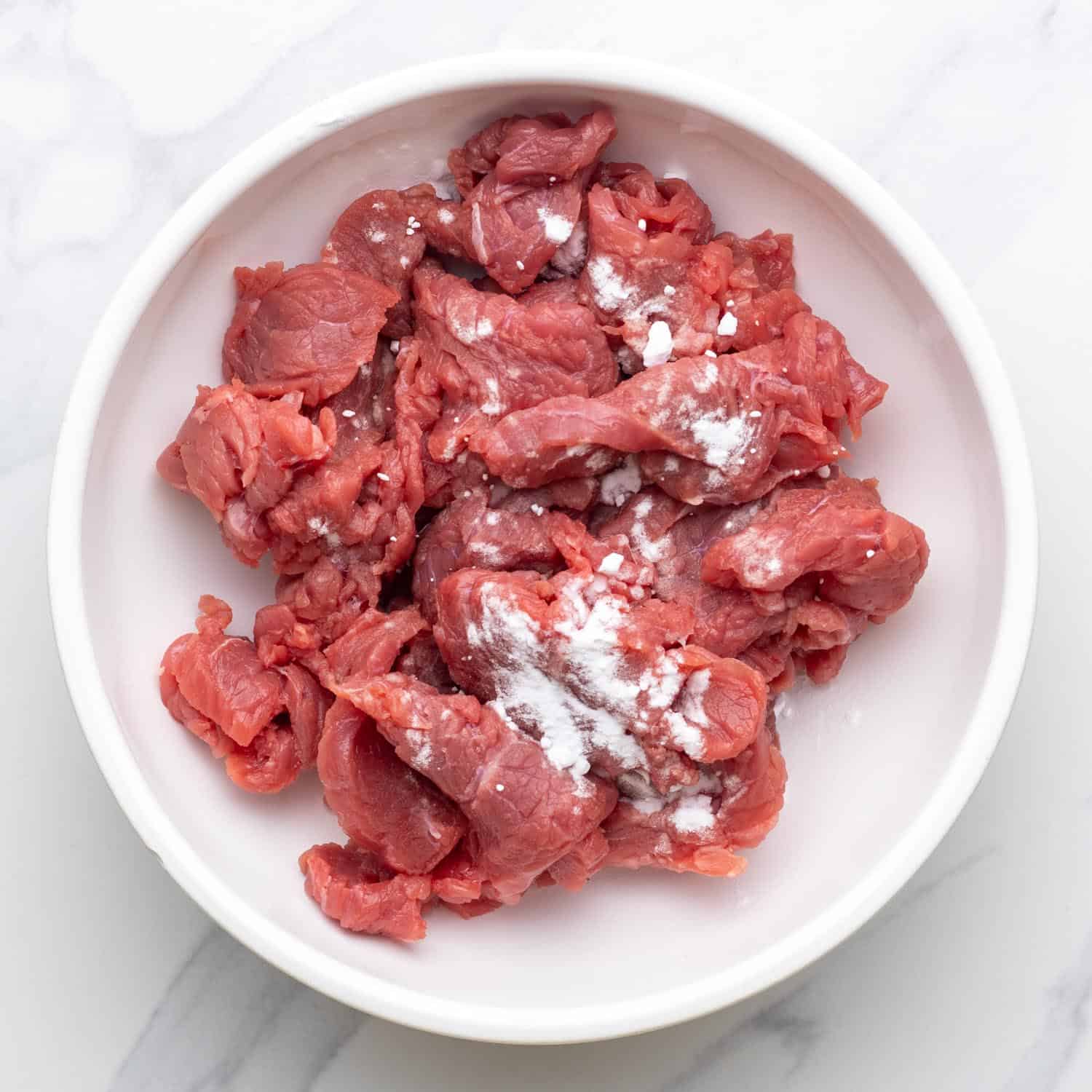 beef strips sprinkled with corn starch in a white bowl.