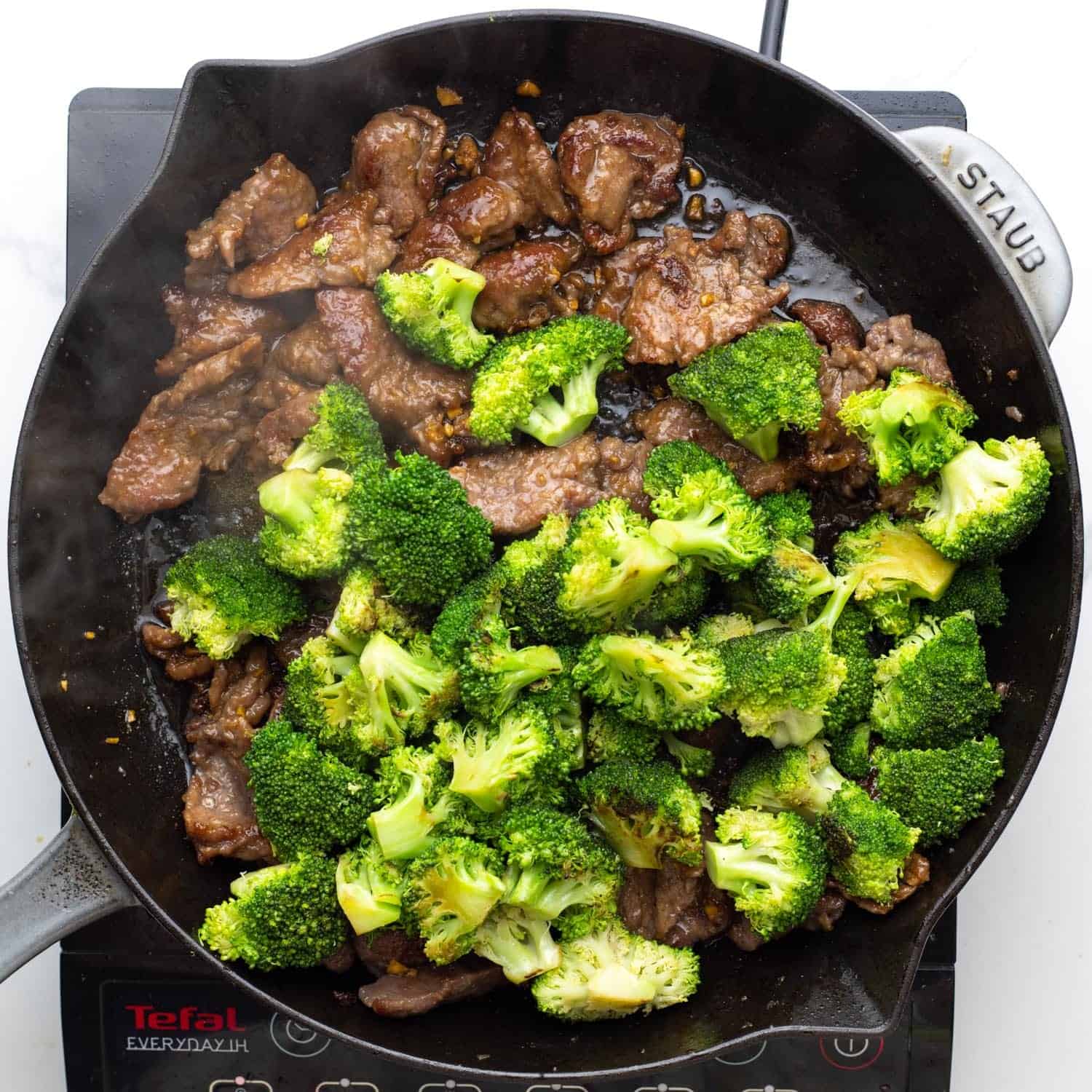 broccoli and beef in a cast iron skillet over an electric burner.