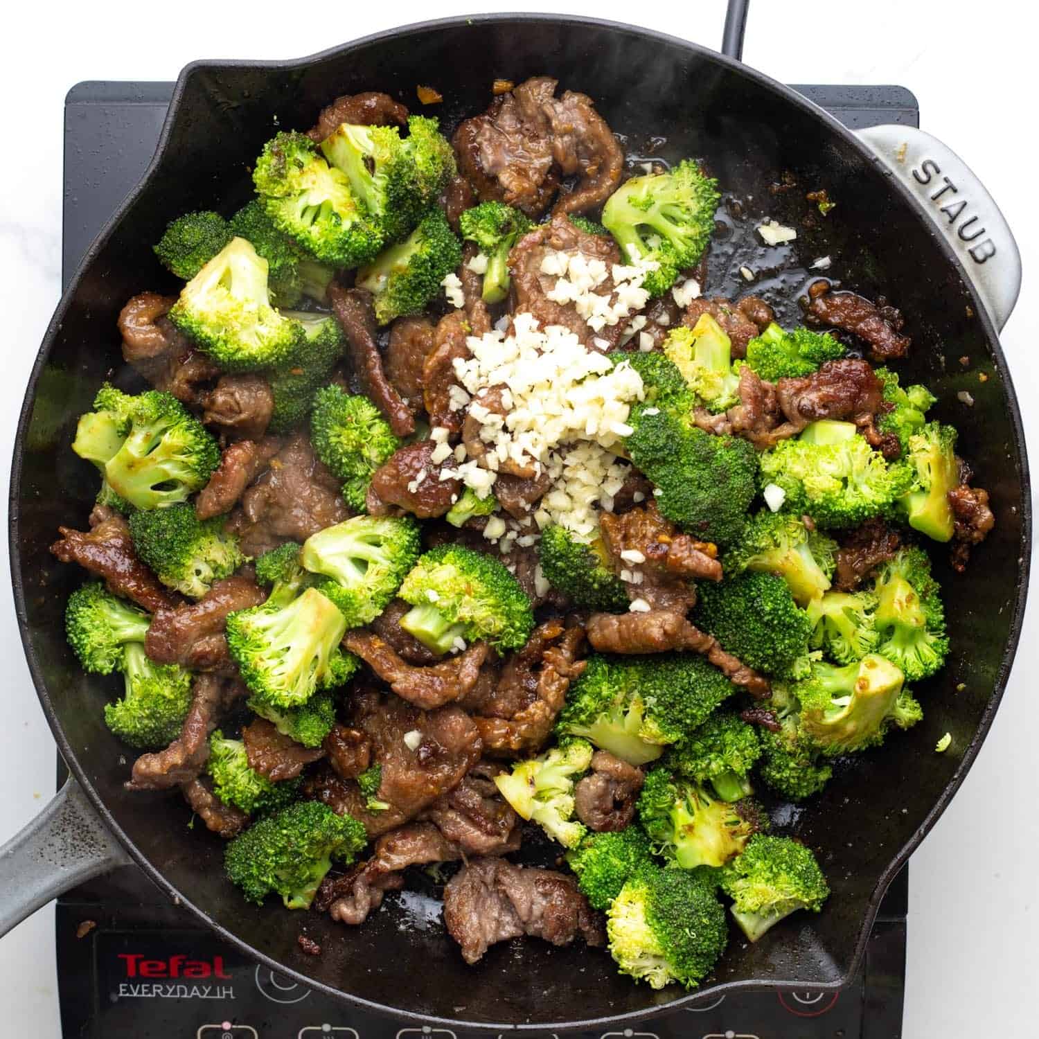 minced garlic added to beef and broccoli in a pan.