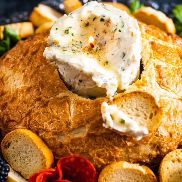 a candle made of herbed butter is inside of a bread bowl. Around the bread are slices of baguette.