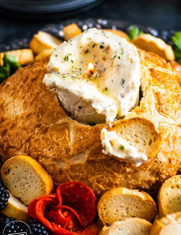 a candle made of herbed butter is inside of a bread bowl. Around the bread are slices of baguette.