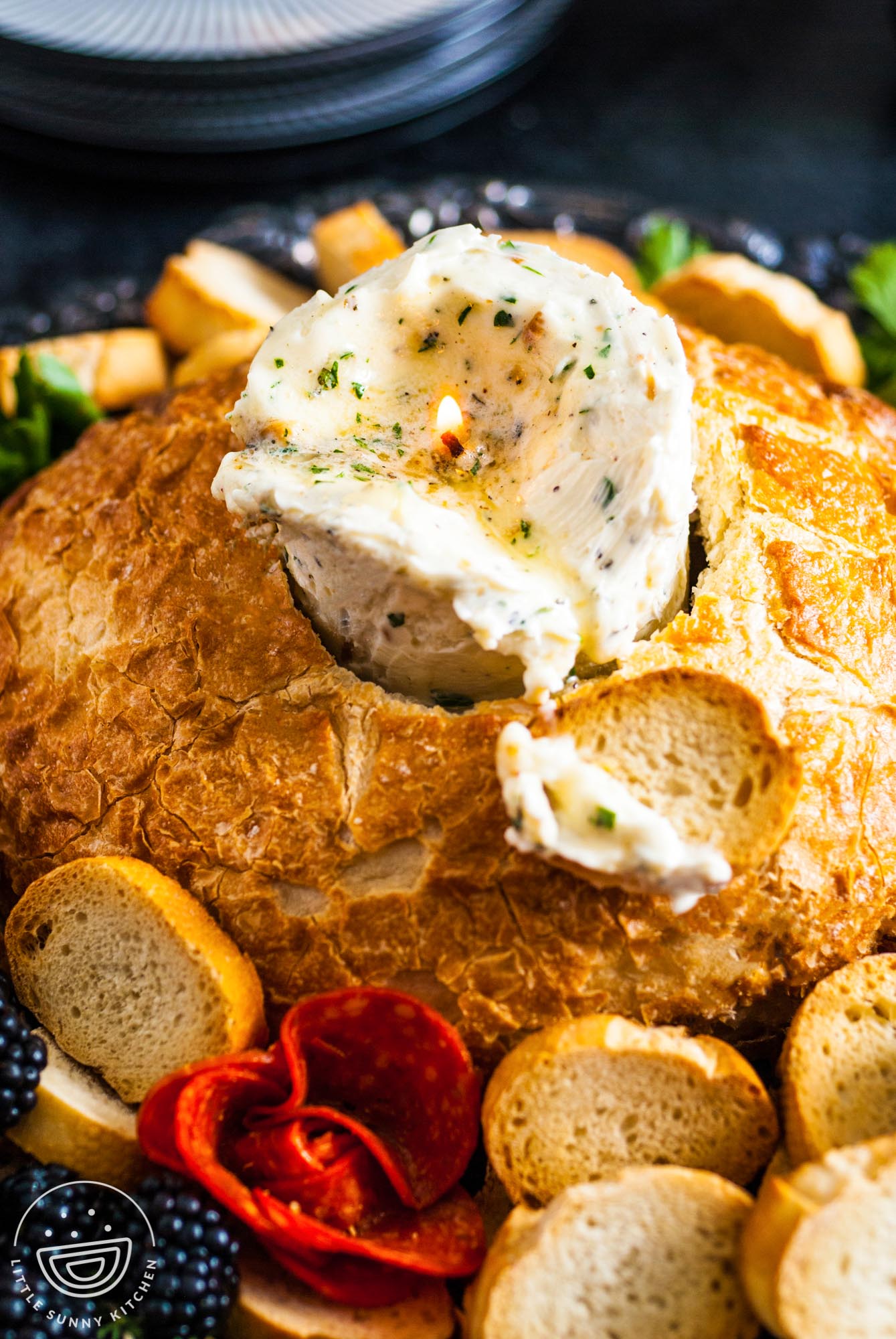 a candle made of herbed butter is inside of a bread bowl. Around the bread are slices of baguette.