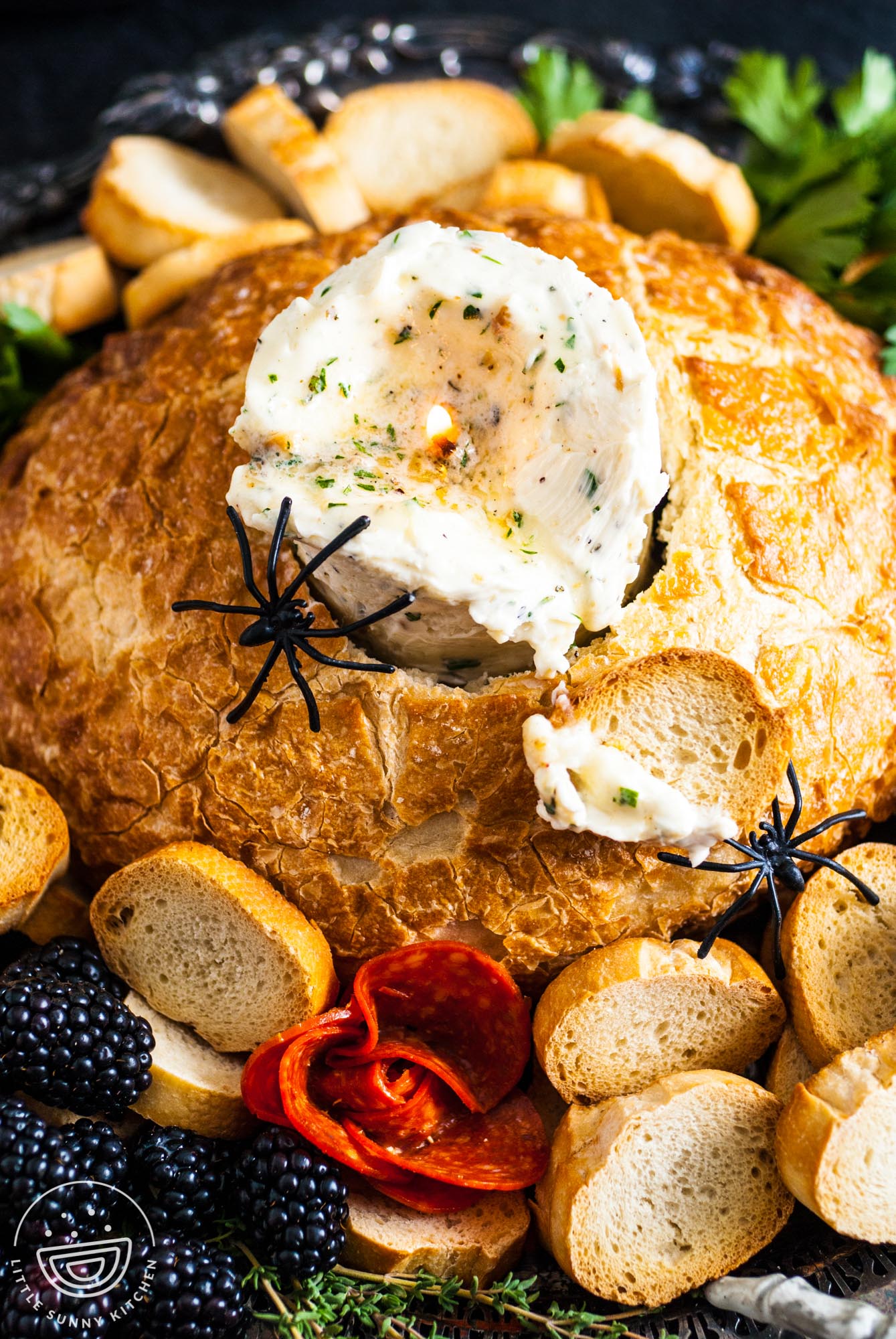 a candle made of herbed butter is inside of a bread bowl. Around the bread are slices of baguette and plastic spiders.