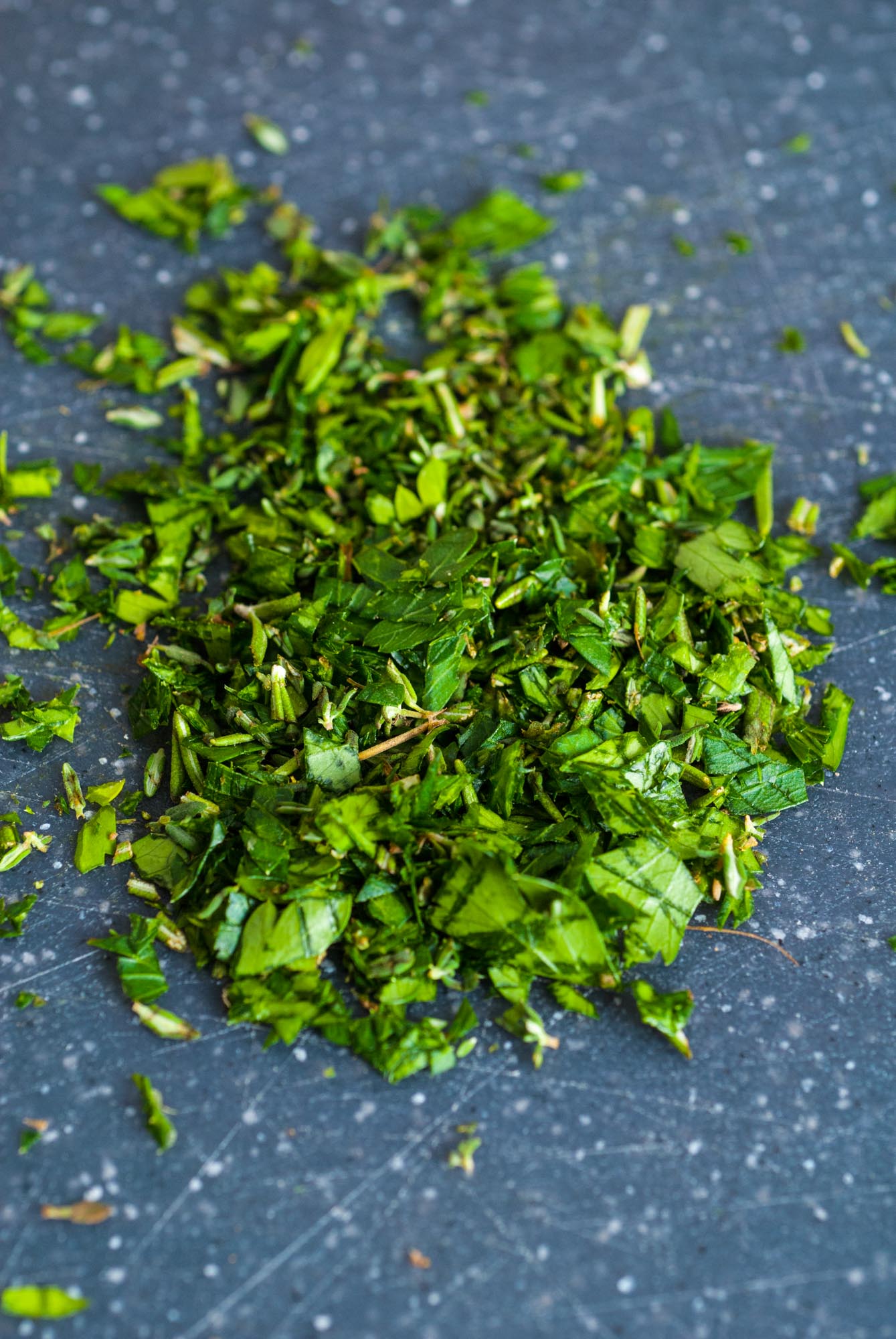 chopped herbs on a dark cutting board.